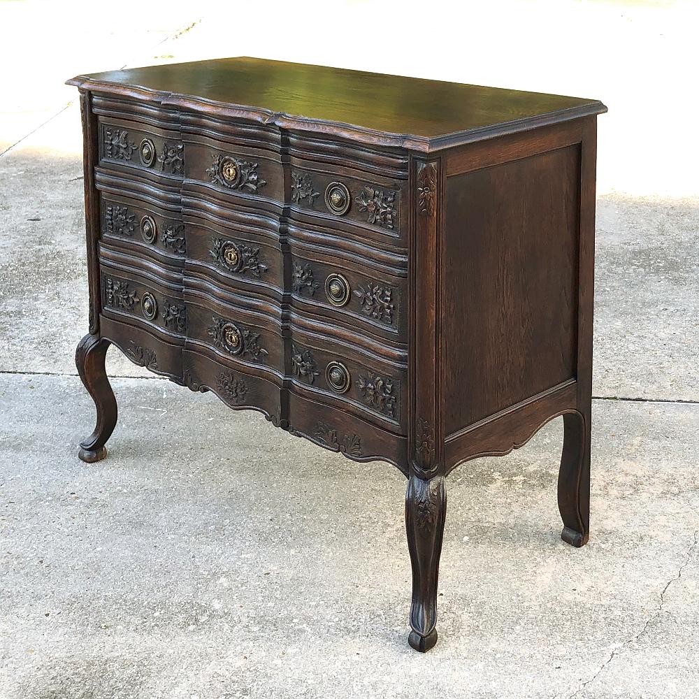 Antique Country French Commode features a Classic contoured facade with a top to match, all supported by scrolled legs below. Foliate motifs dominate the front of the piece, accented by cast brass ring pulls and key guards,

circa early