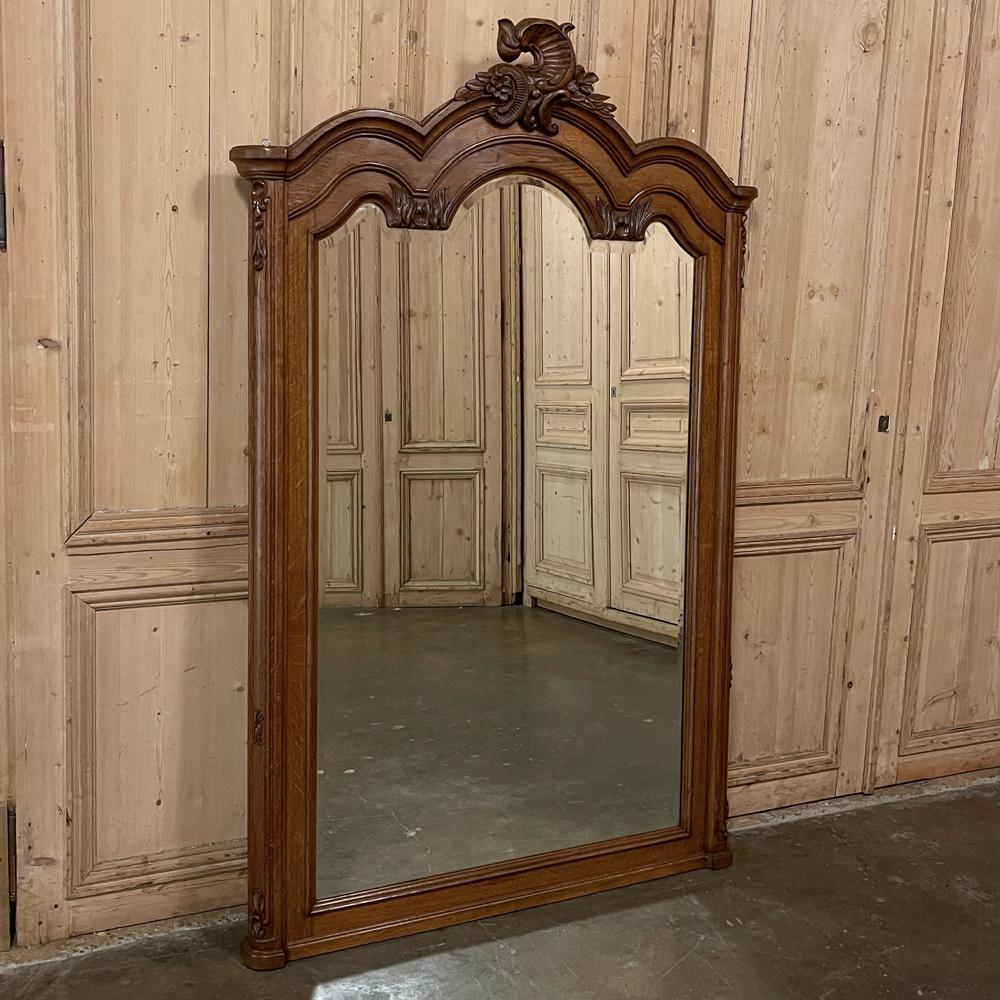 Ce miroir ancien de style Louis XV a été sculpté dans du chêne ancien et présente une splendide interprétation du style Rococo, mais avec un effet plus discret et décontracté. La couronne à triple arche est audacieusement moulée en plusieurs