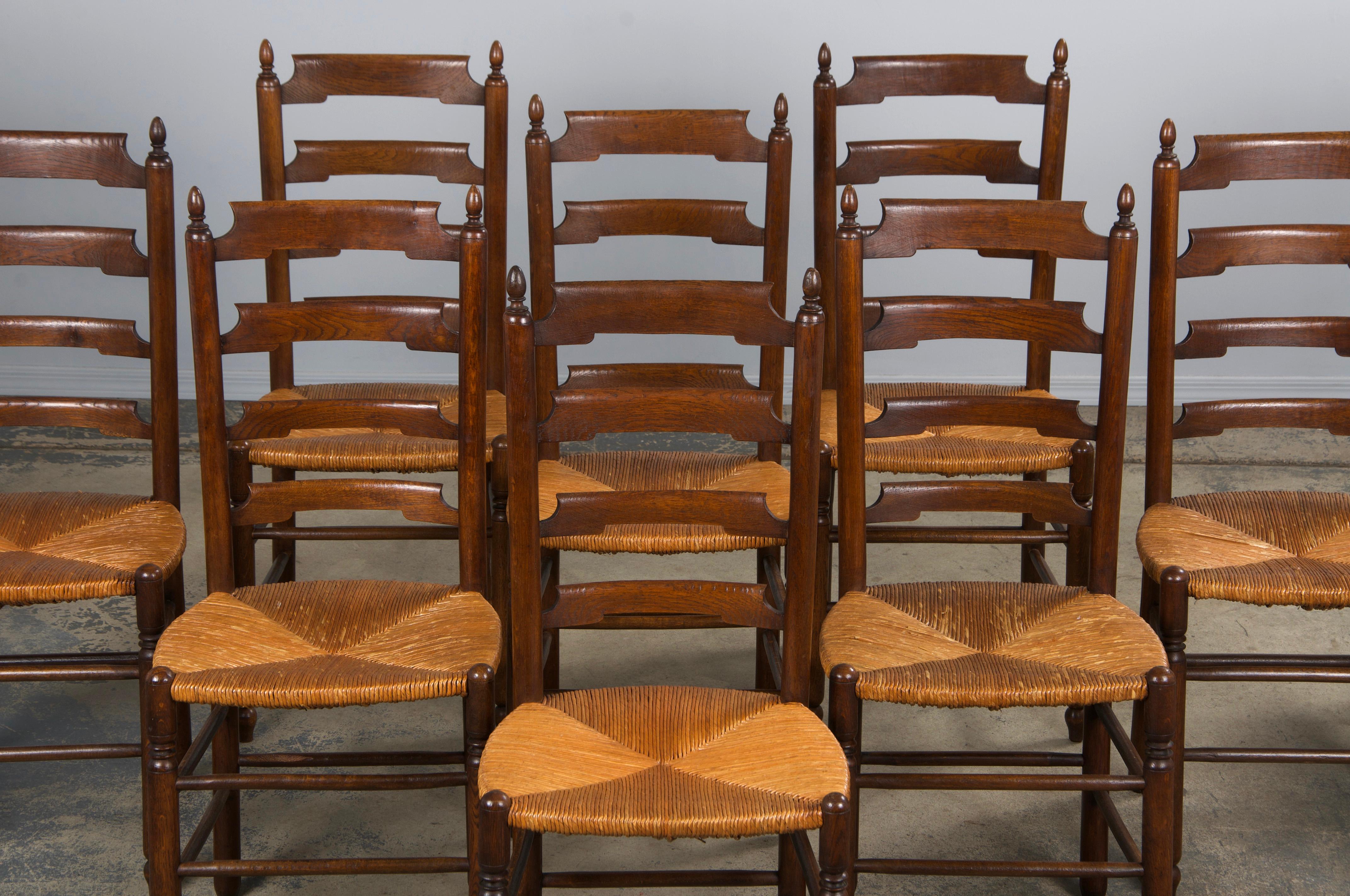 A grand set of ten late 19th-century French Country ladder-back dining chairs, sourced from Provence, France. Beautifully handcrafted from solid oak, these chairs feature elegant ladder-back frames with finials. Structurally restored for stability,