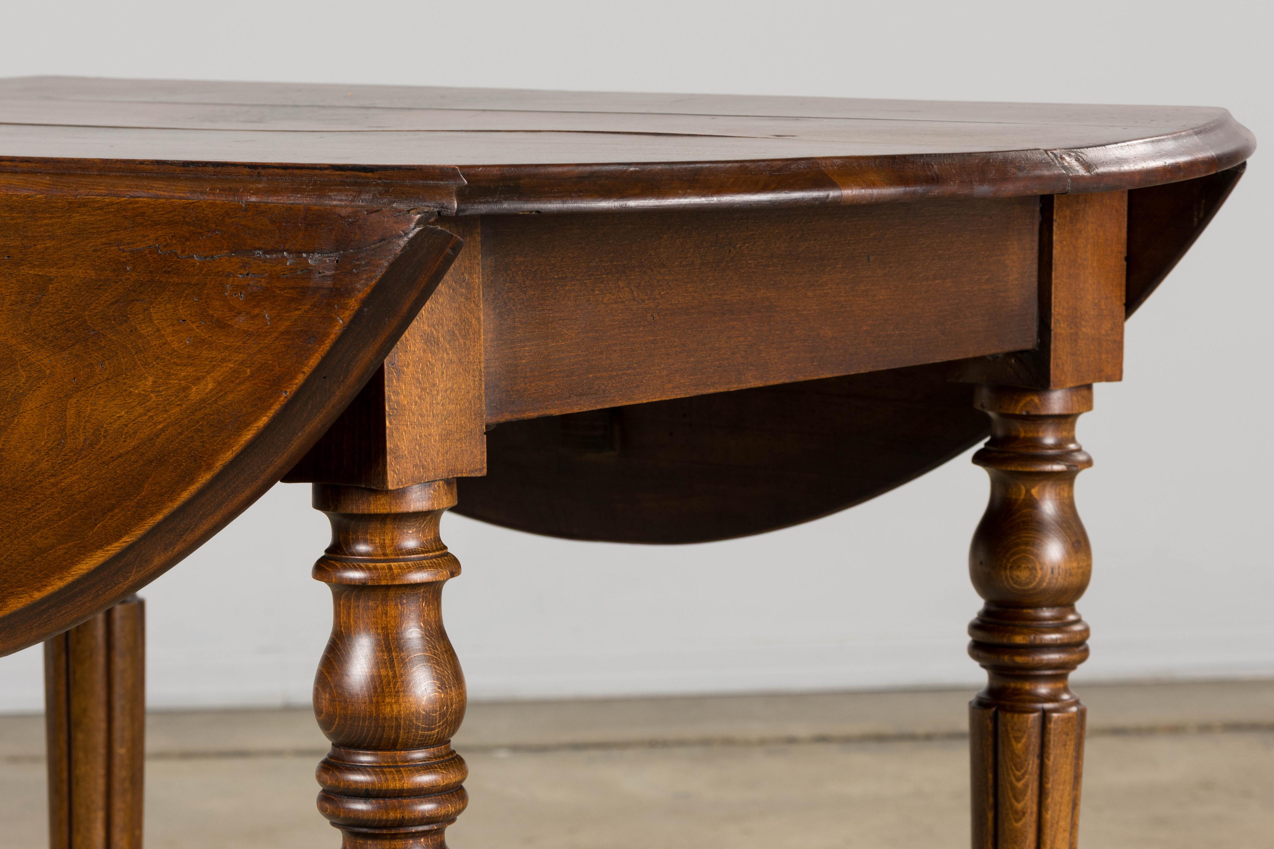 A refined late 19th-century French Provincial drop-leaf table, handcrafted from solid maple and sourced from Provence, France. Recently structurally restored and refinished, the oval planked top is finished in a warm medium-brown tone that enhances