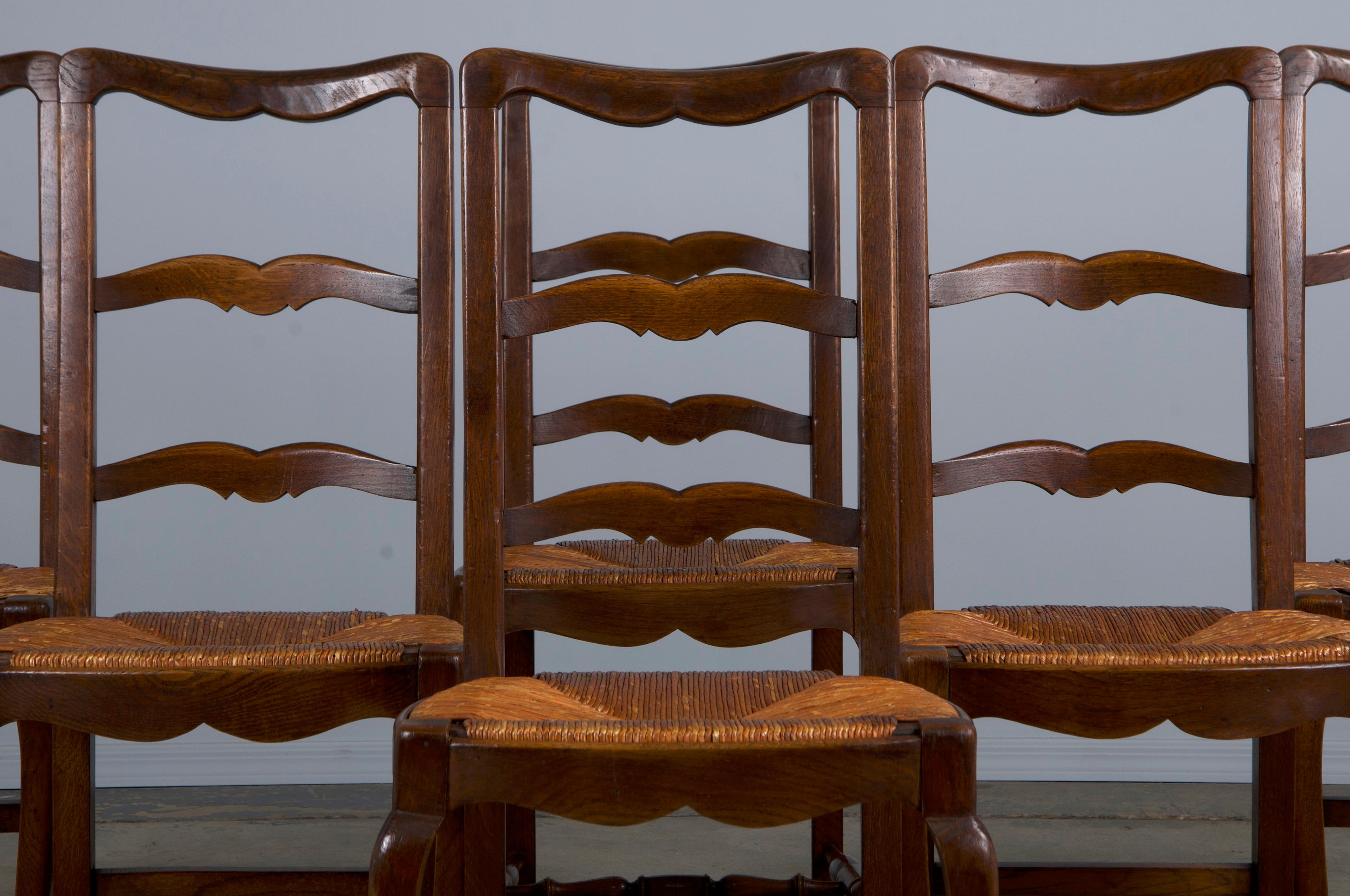 A charming set of six late 19th-century French country dining chairs, sourced directly from Provence, France. Expertly handcrafted from solid oak, these chairs feature an elegant curved ladder-back design. The frames have been structurally restored,