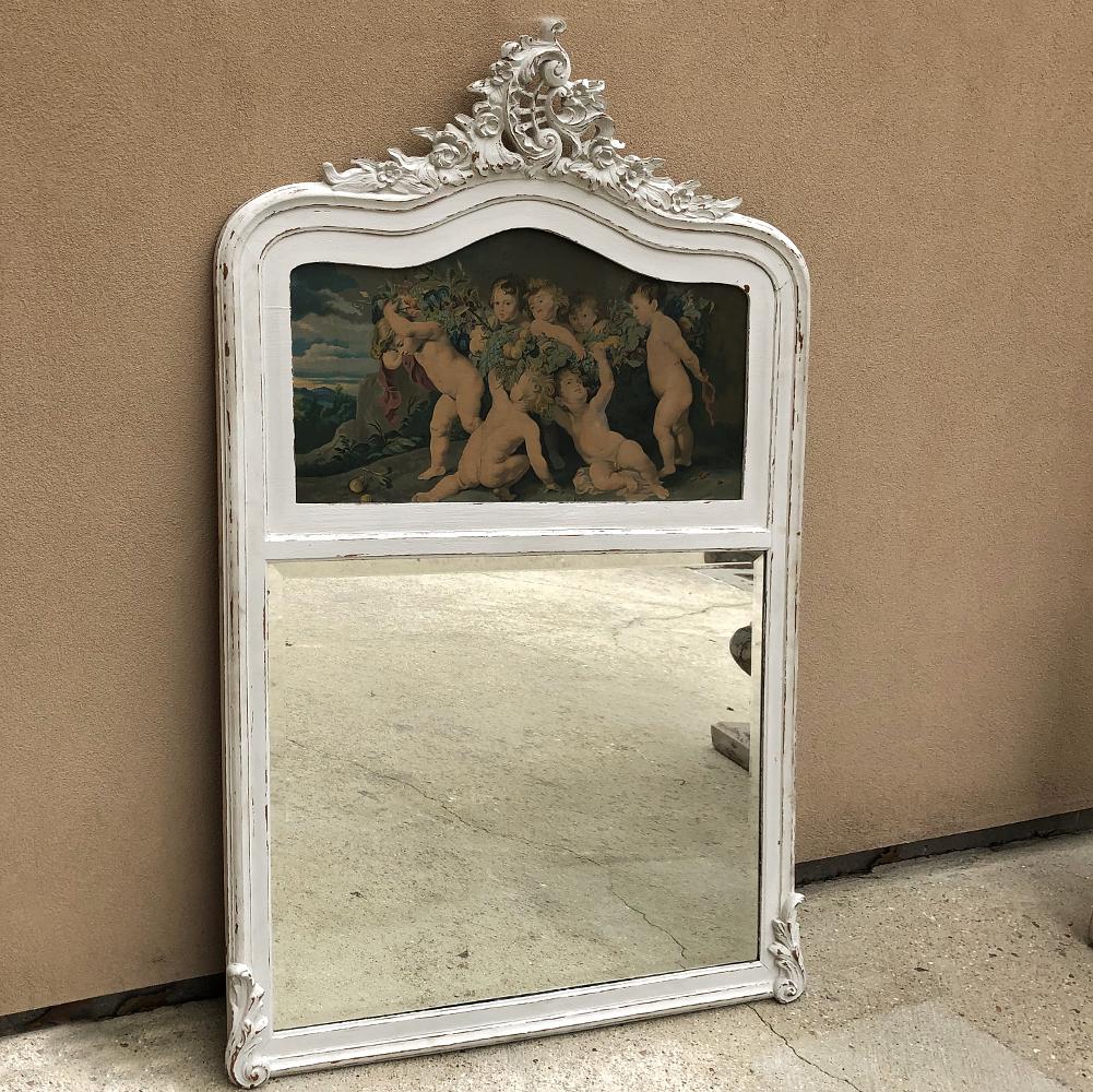 Antique Country French Provincial painted Trumeau features a painted finish that enhances the hand carved Rococo detailing from the arched crown to the framework surrounding the romantic-themed painting. Generously sized mirror and acanthus