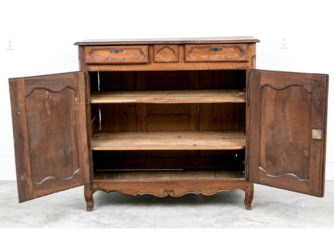 Mueble elaborado con dos cajones de friso que flanquean un motivo de trébol tallado. Grandes puertas dobles con paneles empotrados tallados y perfilados en el clásico estilo campestre francés que se abren a dos largas estanterías. Los laterales