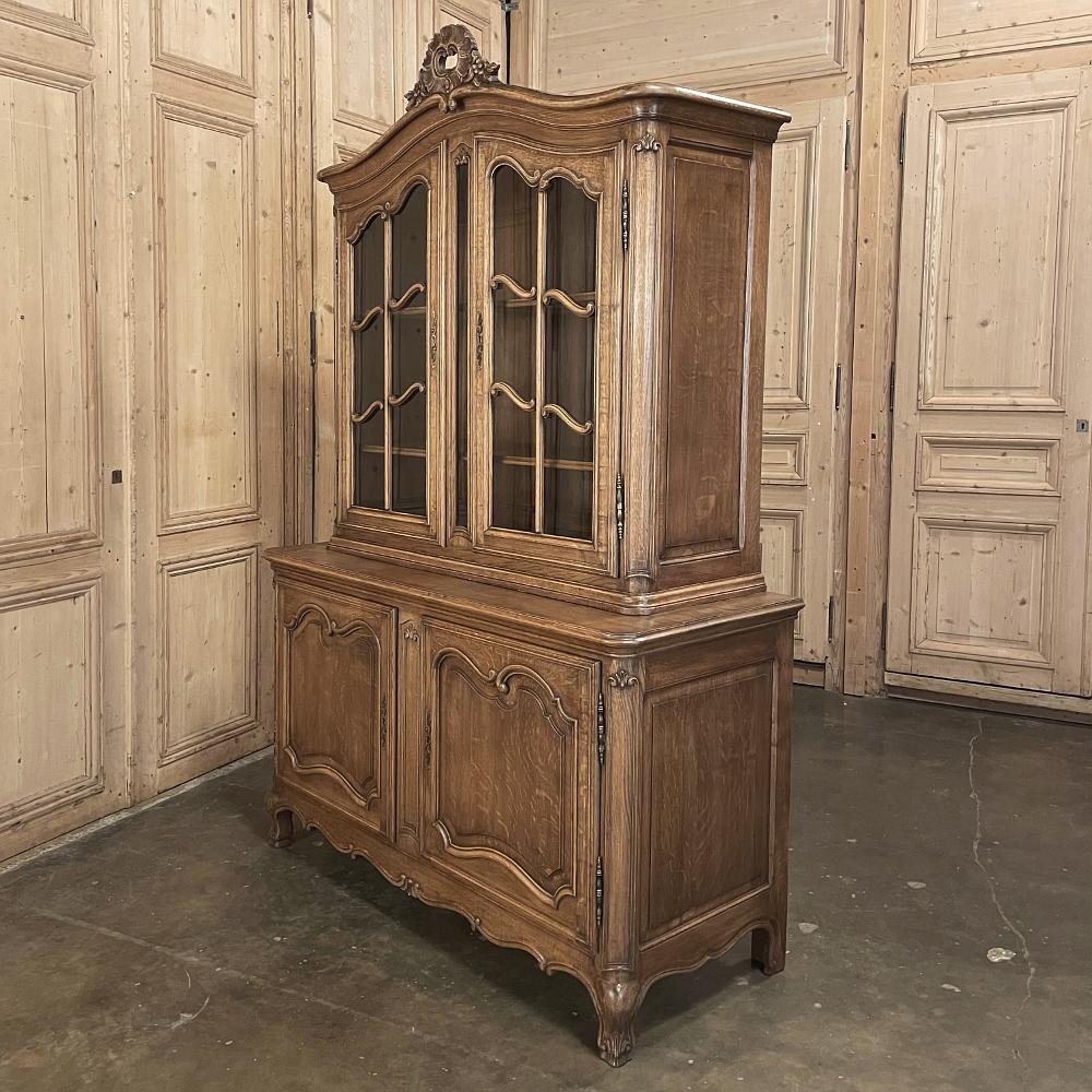 Antique Country French vitrine or bookcase is a definitive example of understated elegance, hand-crafted from solid oak to last for generations! The archer's bow crown on top is centered with a carved, stylized shell and foliate spray, overlooking