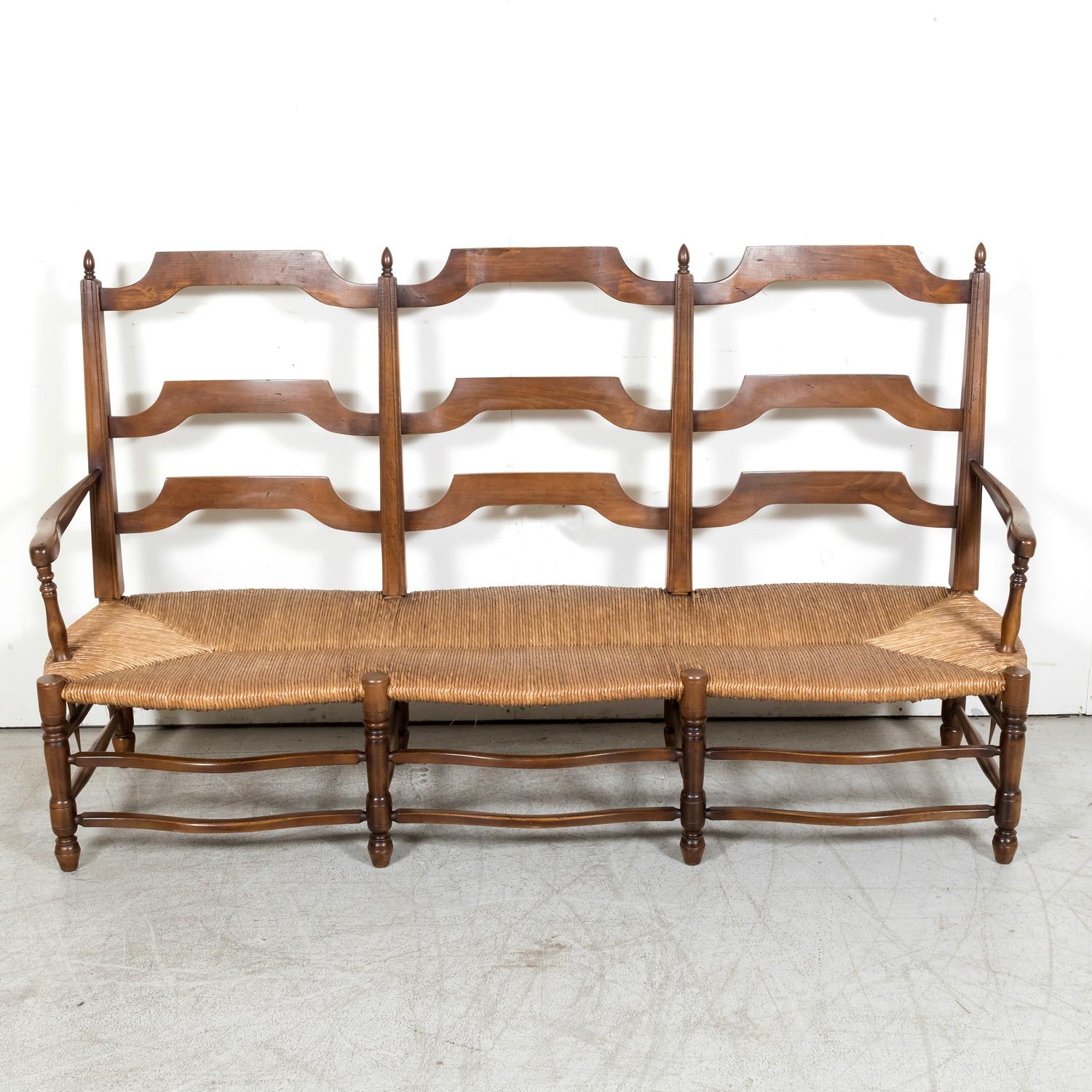 A handsome Country French settee or radassier handcrafted of walnut near Bayeux, a medieval town on the Aure river in the Normandy region of northwestern France, circa 1890s. Featuring a ladder-back design and handwoven rush seat that seats three,