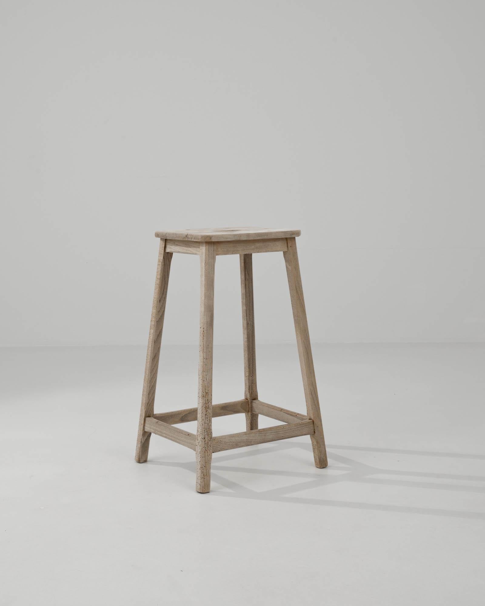 Simple yet charming, this country bar stool makes a delightful vintage accent. Built in France circa 1900, featuring splayed legs joined by square stretchers and assembled with mortise and tenon joints. This distinctive trapezoid stance gives the