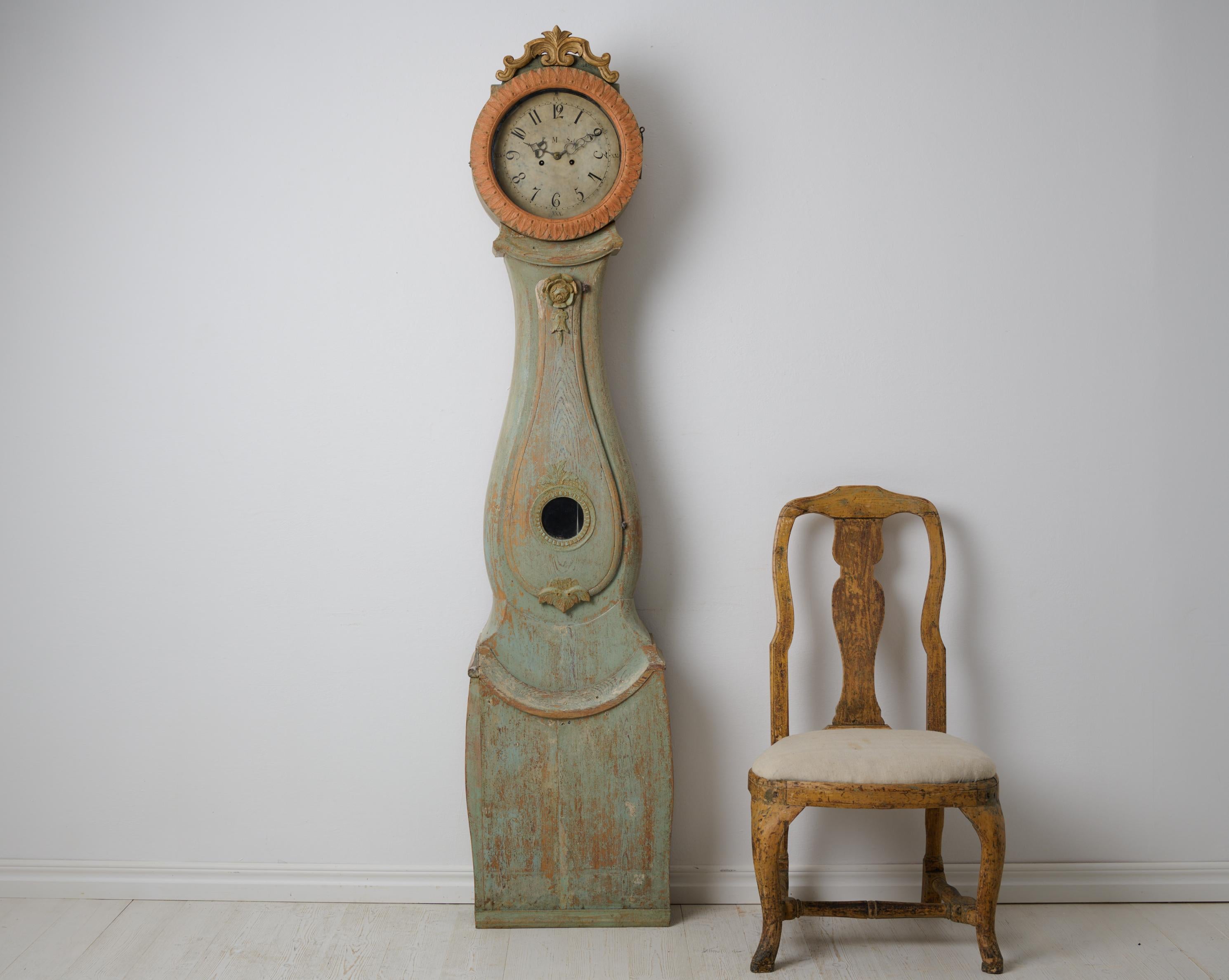 Country long case clock in rococo style from northern Sweden. This clock is a genuine antique from around the 1820s. The carved wooden decor is original and the paint is also original with authentic distress. The clock comes with the original
