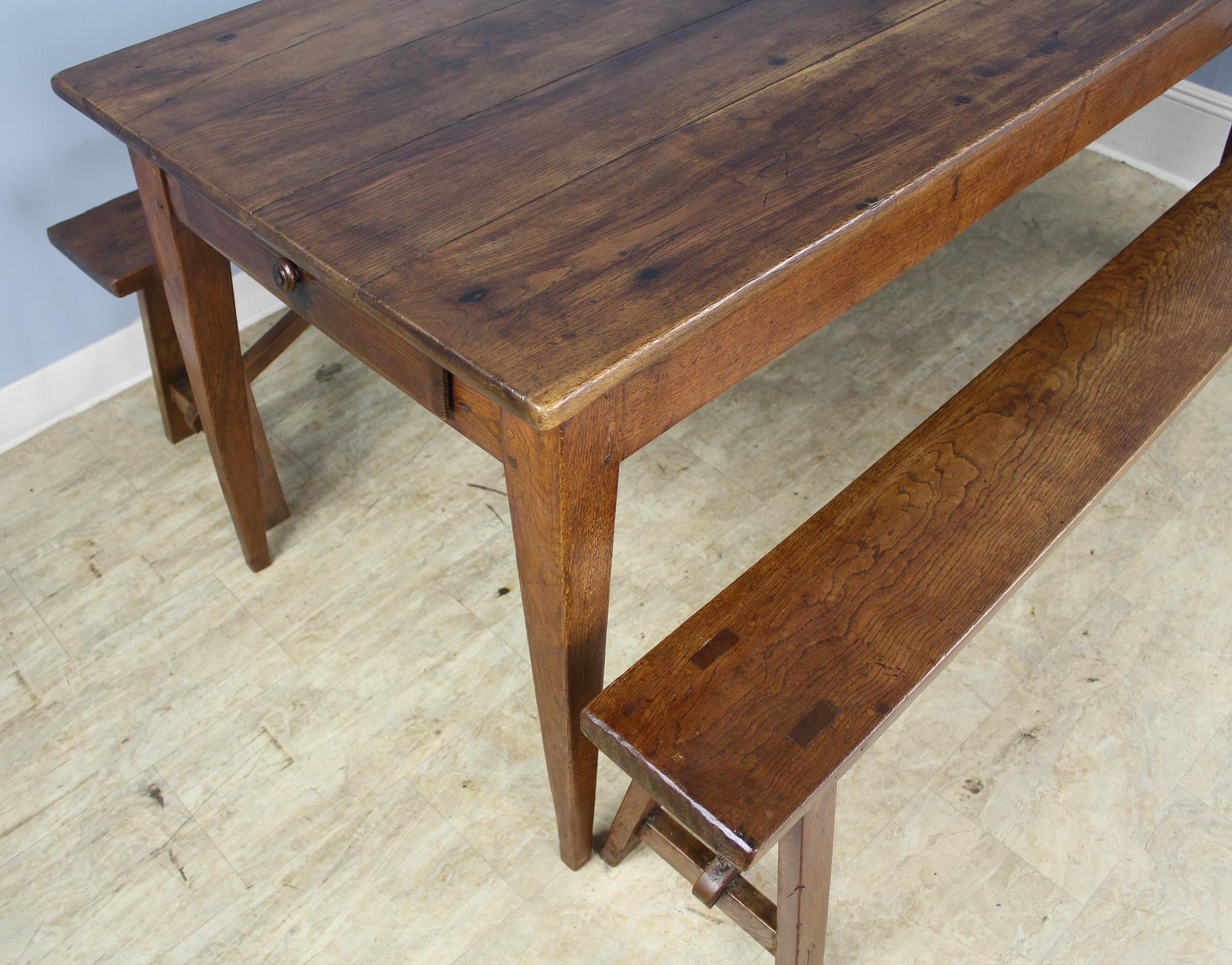 A good country oak farm table with classic tapered legs, pegged nicely at the apron. The top has a warm glowing patina with attractive grain. The two benches are the same length as the table, with similar color and oak grain. We rarely see
