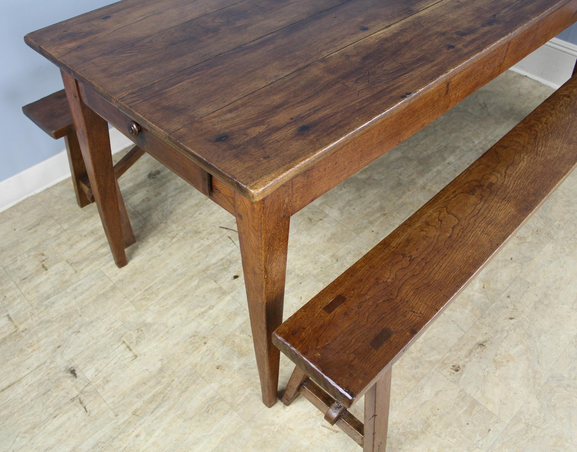 Un buon tavolo da campagna in Oak con le classiche gambe affusolate, ben incastrate nel grembiule. Il piano ha una patina calda e luminosa con venature attraenti. Le due panche sono della stessa lunghezza del tavolo, con colori e venature simili a