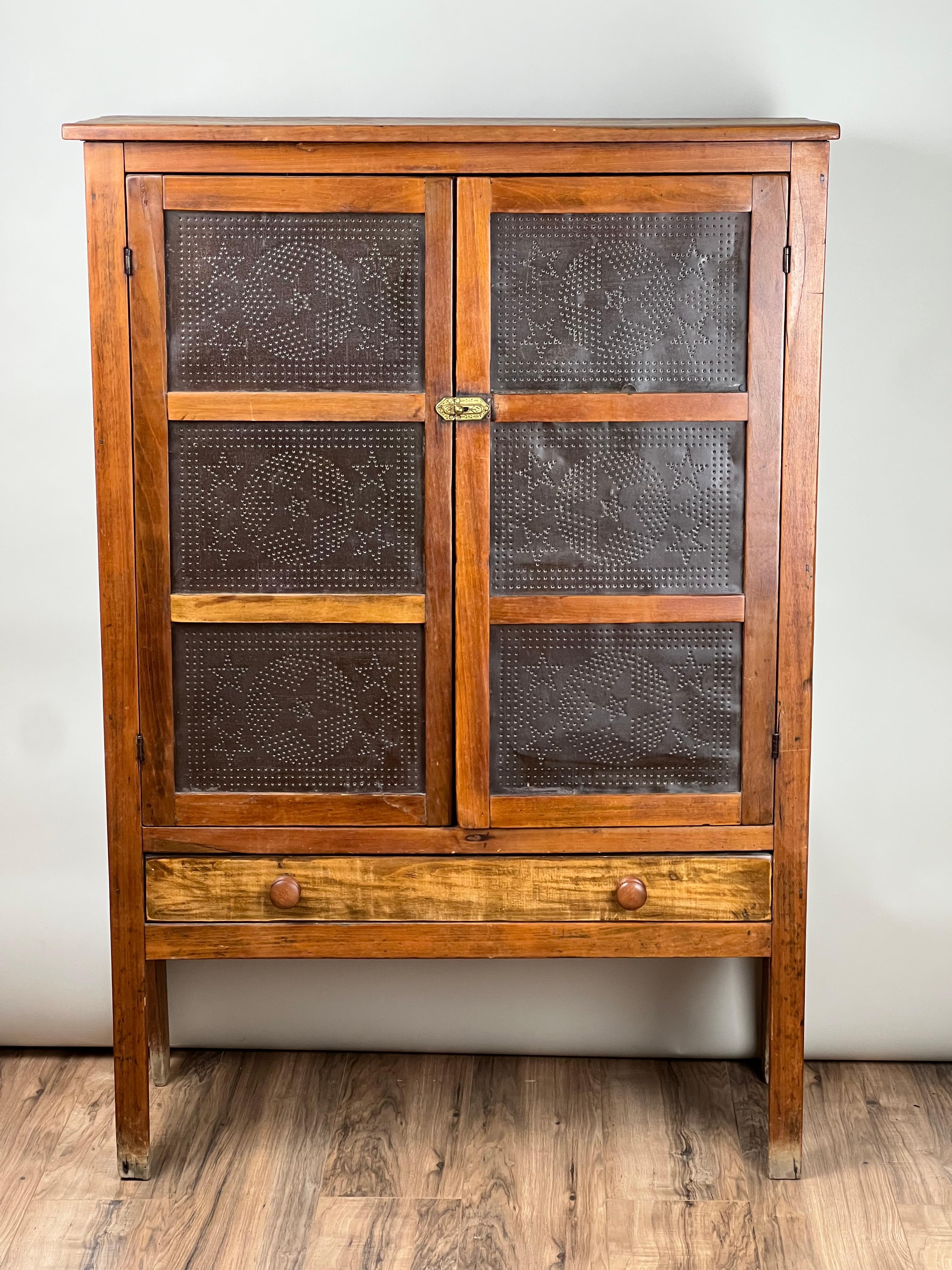 Ce coffre à tarte ancien en pin et en étain poinçonné, c. Début du XIXe siècle, est un charmant exemple de mobilier populaire utilitaire conçu pour la fonctionnalité autant que pour la beauté. La pièce présente une paire de portes en fer blanc