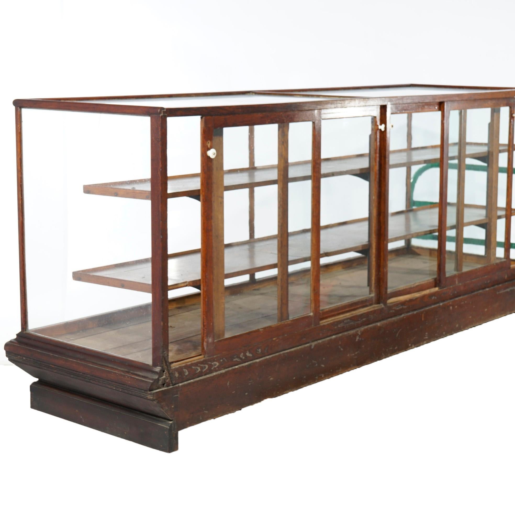 Une ancienne vitrine de magasin de campagne offre un cadre en chêne avec des portes en verre coulissantes, un intérieur à étagères et une base conique, vers 1900.

Mesures- 41.5''H x 94.25''W x 28.5''D