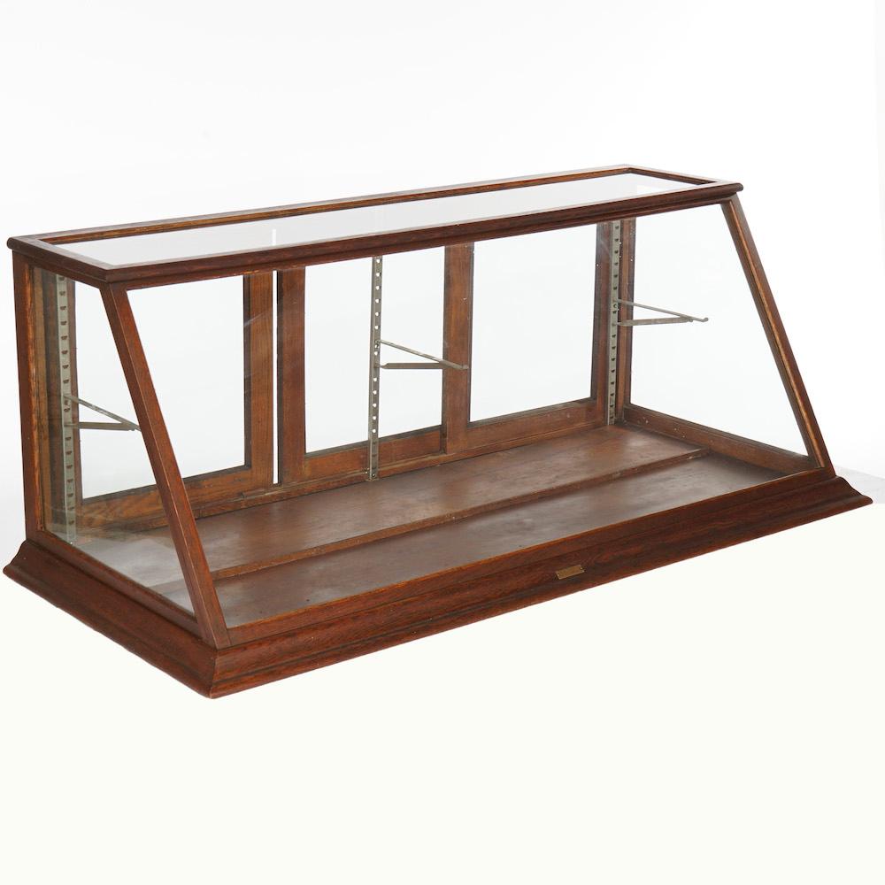 An antique country store table top display cabinet by Sun MFG. Co. offers oak frame in slant front form with interior adjustable shelf brackets, maker plaque as photographed, c1900

Measures- 23.25''H x 59.75''W x 26''D.