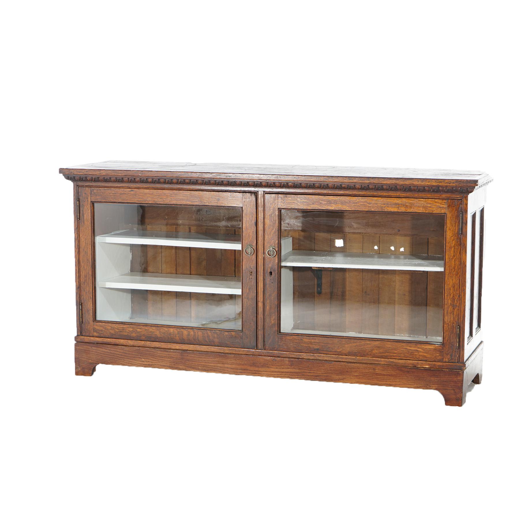 76407 - ATW An antique country store display showcase offers quarter sawn oak construction with paneled sides, carved molding, double glass doors opening to shelved interior and raised on bracket feet, c1900

Measures - 31