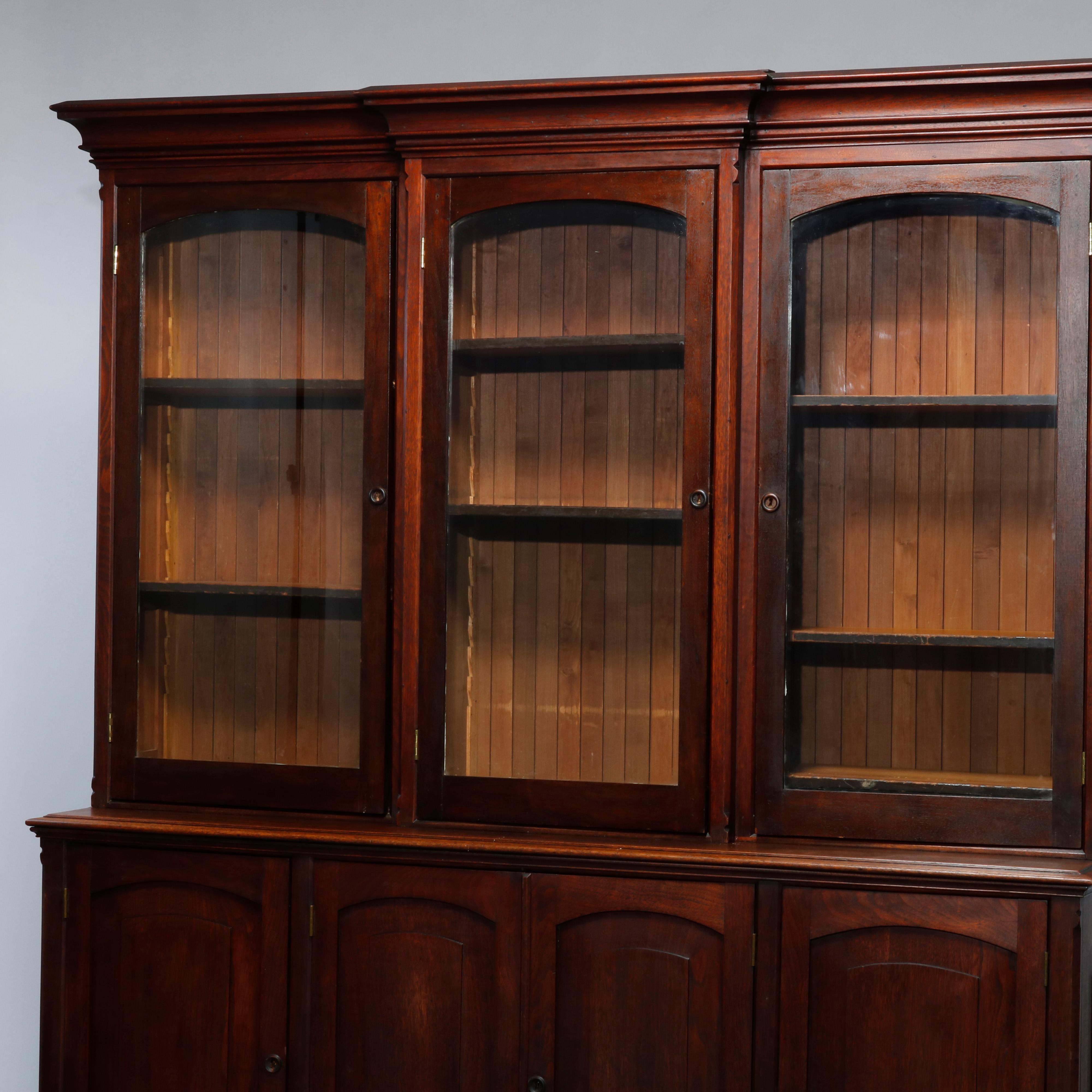 An antique country store display case offers mahogany construction with upper cabinet having three glass door with arced panels opening to shelved interior; lower case with paneled doors opening to storage with shelves and smaller drawers,