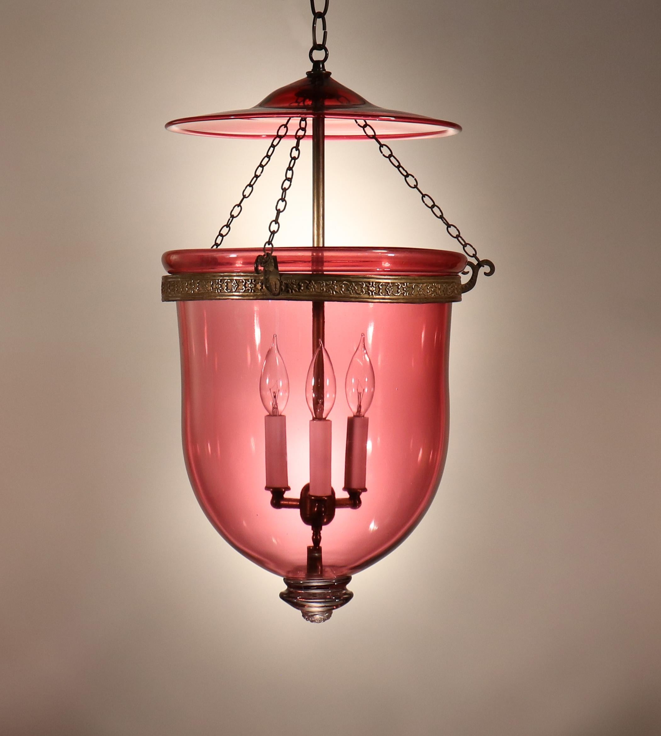 An exquisite cranberry glass bell jar lantern with its original embossed brass band, smoke bell/lid, and chains. This circa 1870 English lantern is generously sized, possesses lovely form, and has several desirable air bubbles in the hand blown