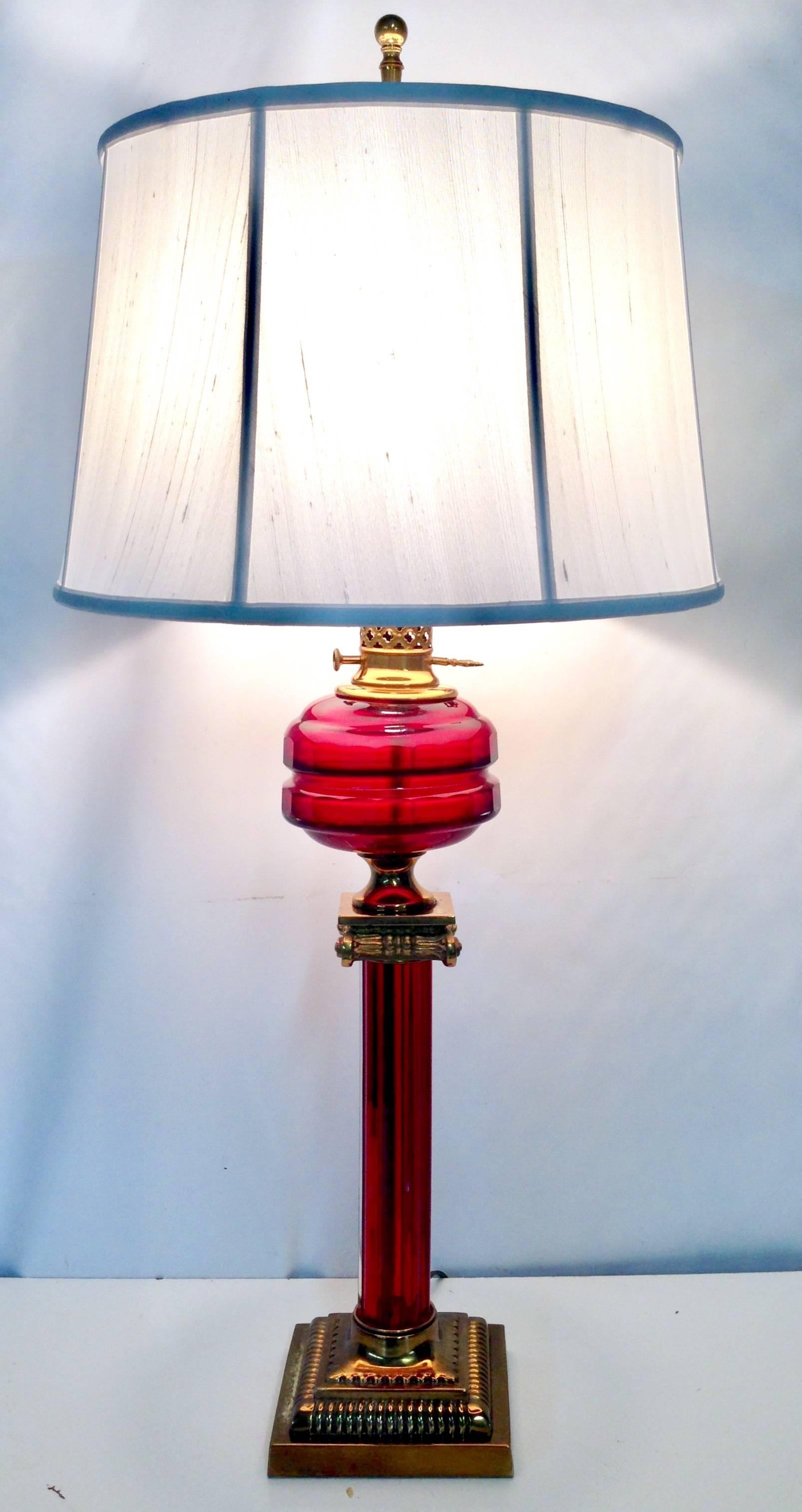 Antique Cranberry blown glass column lamp with polished solid brass accents. This fluted oil style lamp features original brass fittings. Includes a brass harp and finial. Height  to socket, 27.5