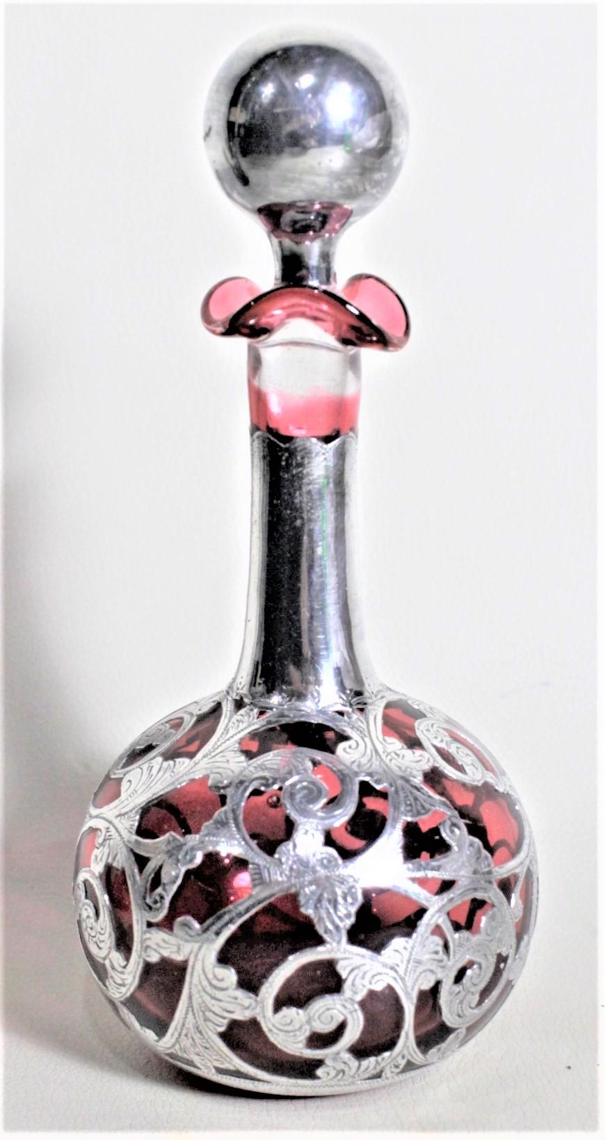 This antique silver overlaid perfume or scent bottle is unsigned, but presumed to have been made in England in circa 1935 in an Art Deco style. The cranberry glass bottle is covered with 650 silver and engraved with a leaf and flower design. The