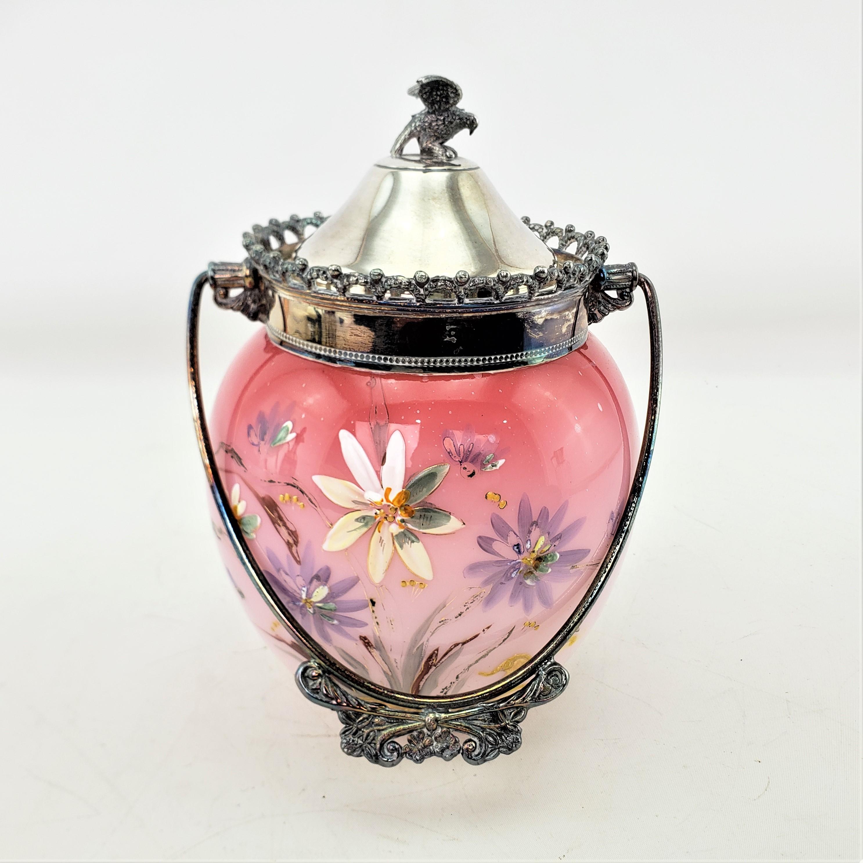 This antique biscuit barrel is unsigned, but presumed to have originated from England and date to approximately 1880 and done in the period Victorian style. The body of the barrel is done with a cranberry and cream artglass with hand-painted flowers