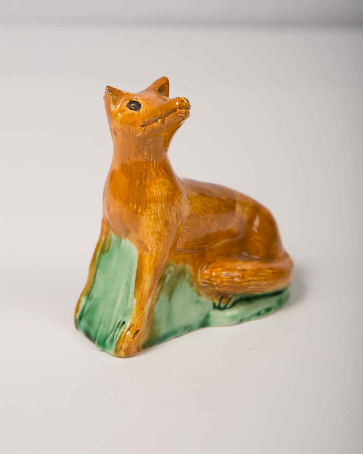 A late 18th century small creamware figure of a fox pressed out in a mold and hollow on the inside in the 18th century creamware style. Made in England, circa 1790. We can see the brushstrokes of the orange glaze on the fox's coat. His eyes are