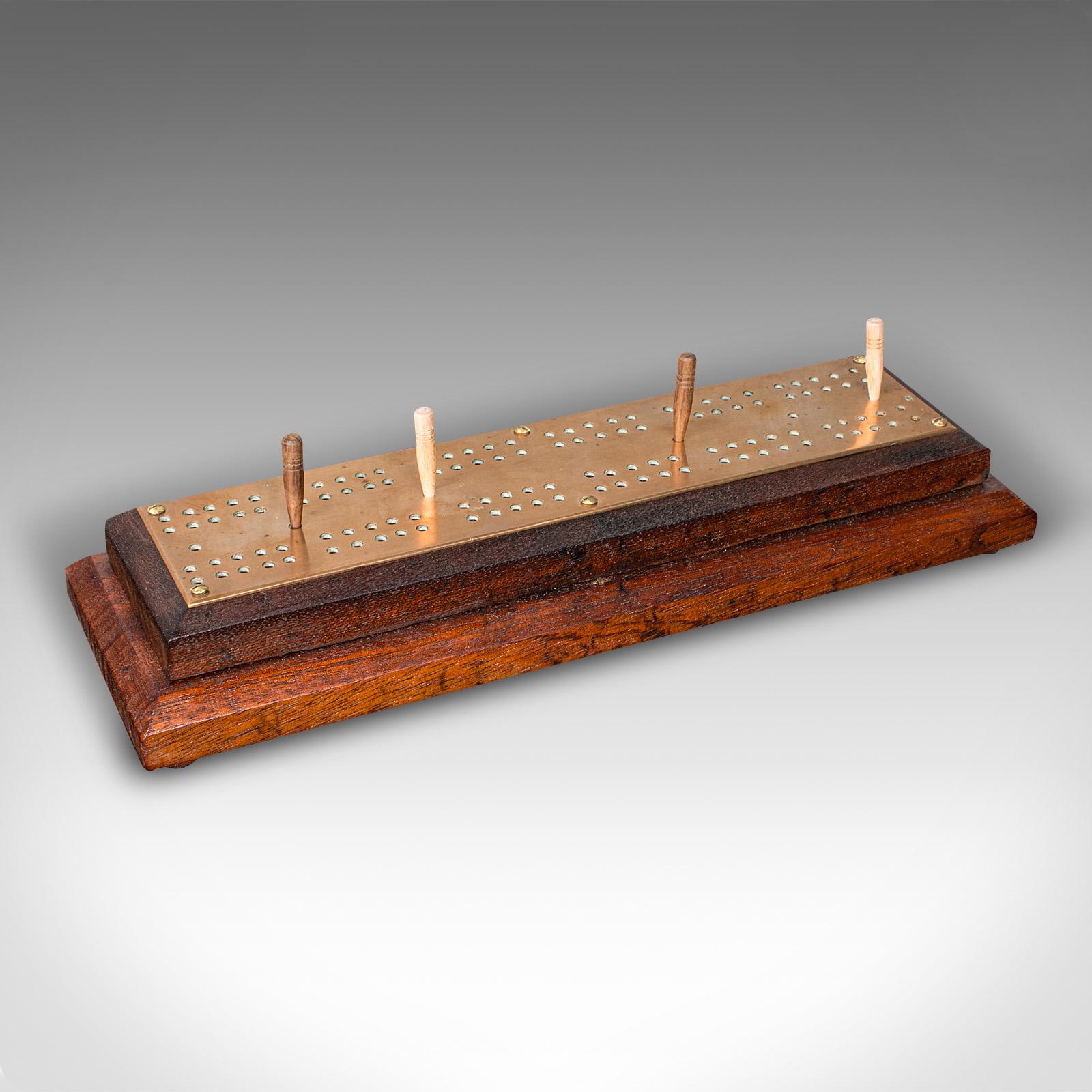 
Questa è una tavola da Cribbage antica. Un tabellone per giochi di carte inglese, in quercia e ottone, con custodia per i birilli, risalente ai primi anni del XX secolo, circa 1920.

Attraente tavolo da gioco portatile, con accattivante finitura in