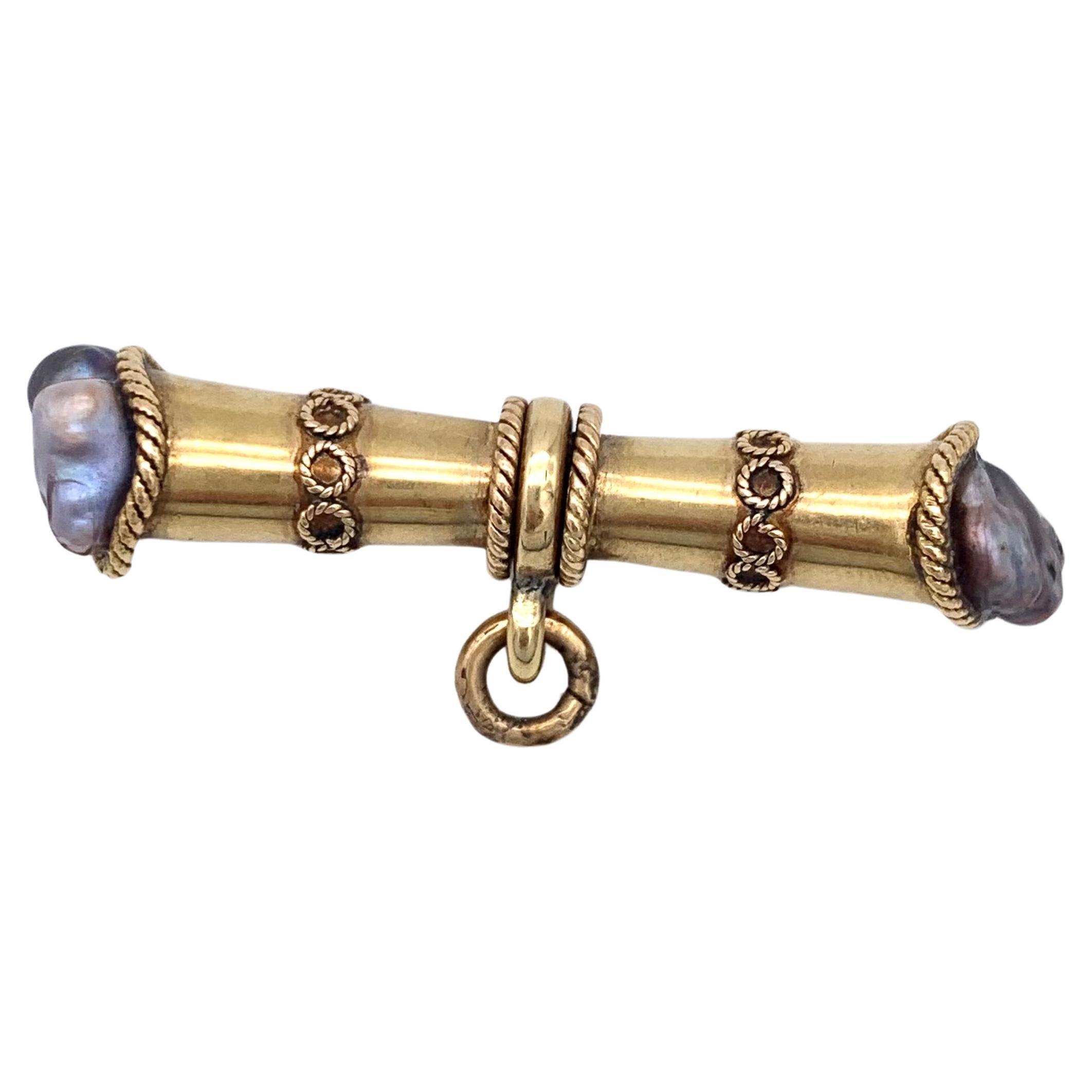 Este travesaño está diseñado como un hueso estilizado y fabricado en oro de 15 quilates. Está decorada con aplicaciones de alambre de oro trenzado alrededor de los bordes y a ambos lados del anillo giratorio que se unirá a una cadena. Cada extremo