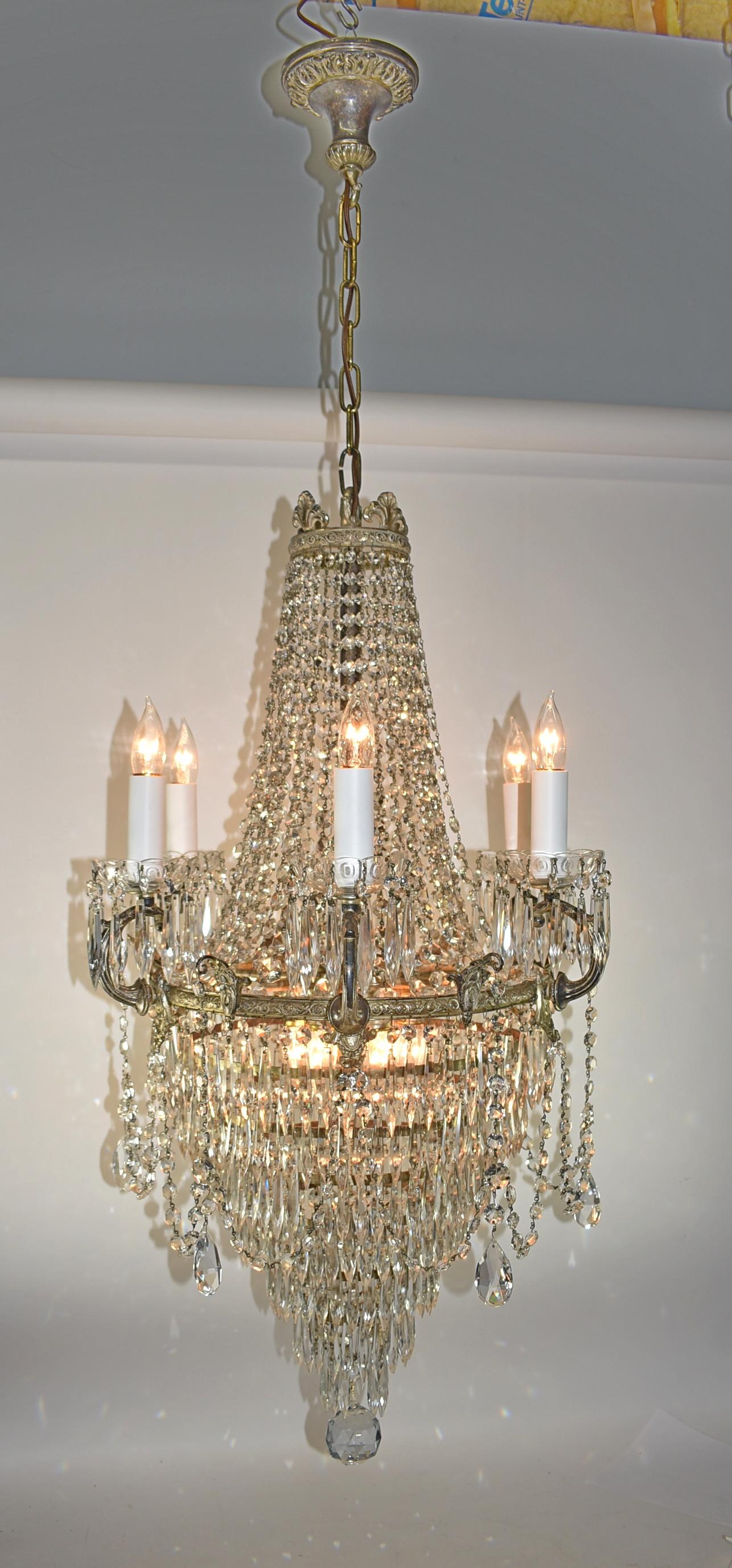 Antique Crystal and Brass Chandelier. circa 1910. Waterfall chandelier with 7 tiers of graduated circles with hanging crystal prisms and draped crystals, 12 sockets total, 6 inside sockets and 6 candle sockets. All original distressed Silvertone