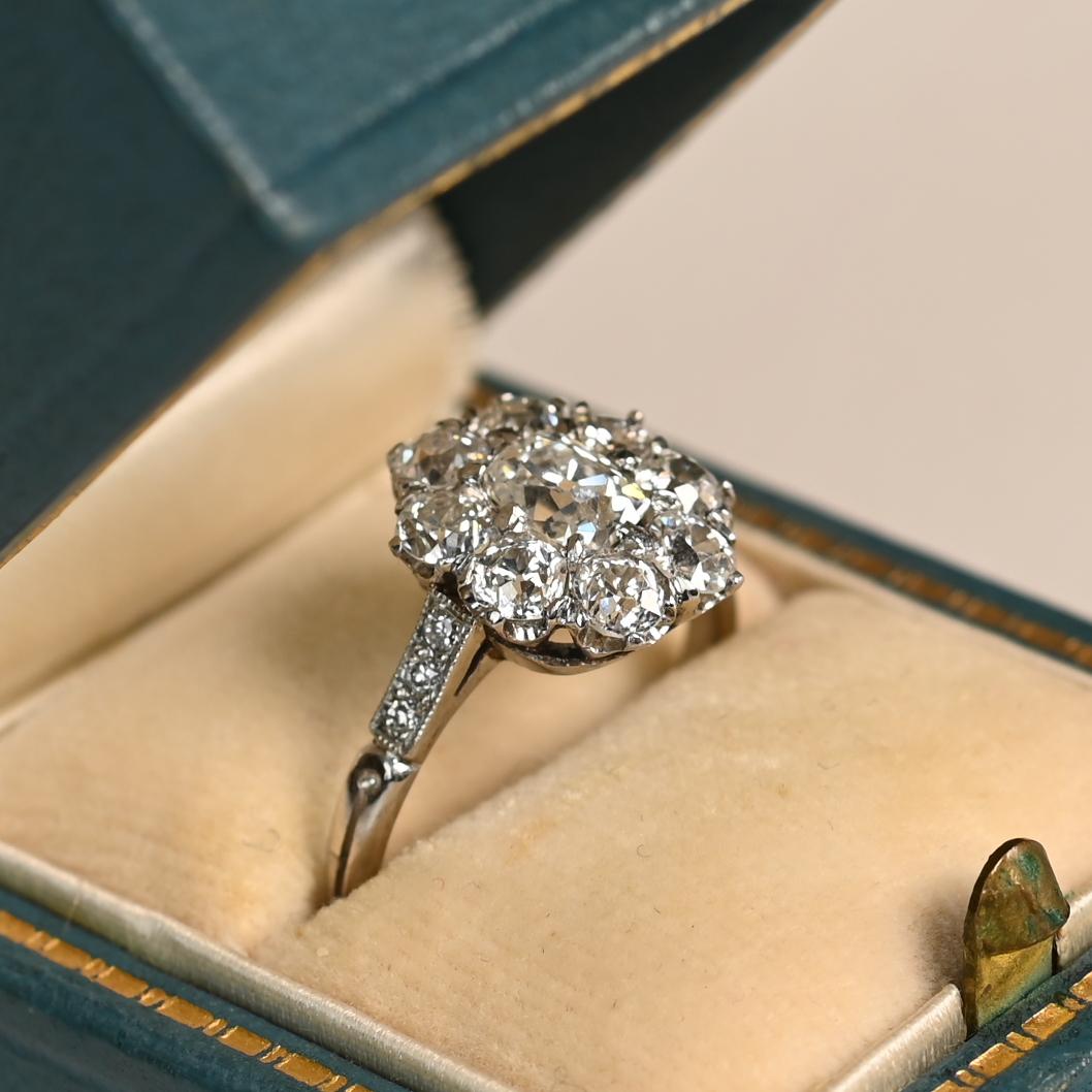 Cette exquise bague de fiançailles en grappe d'inspiration antique met en valeur un remarquable diamant allongé de taille coussin antique en son centre, pesant environ 0,60 carat. La pierre centrale est élégamment encadrée par un halo de diamants