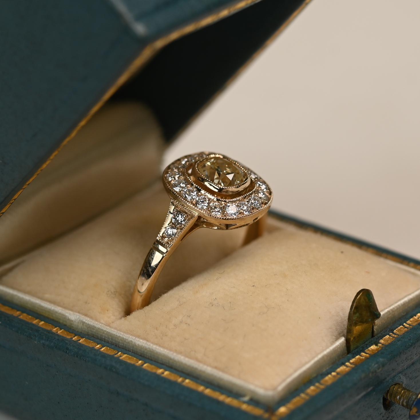 Questo anello presenta un antico diamante taglio cuscino del peso di circa 0,50 carati, di colore L e purezza VS1. Il diamante è incastonato al centro e incorniciato da un'aureola di scintillanti diamanti taglio vecchio europeo. Due ulteriori