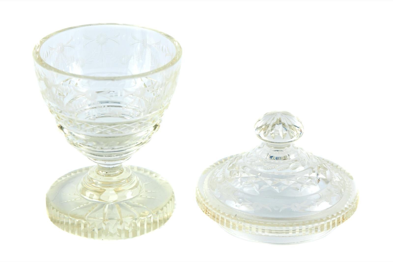 Se vende este antiguo tarro de cristal tallado de mediados del siglo XIX, con tapa original de cristal tallado, rematada por un remate estriado con decoración foliada grabada y apoyada sobre un pie circular escalonado de cristal tallado.