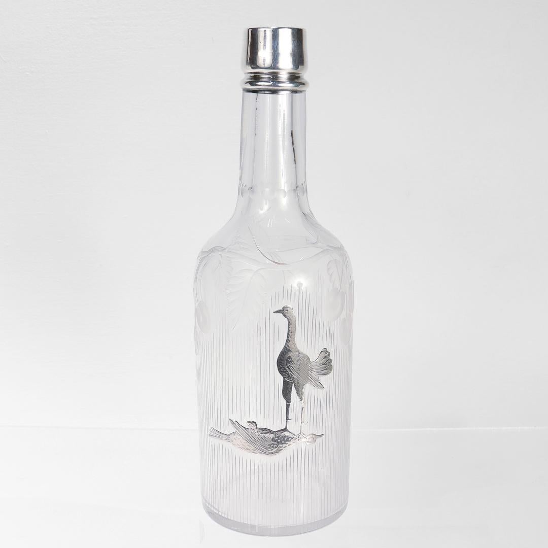 A fine antique bar back bottle or decanter.

In blown glass with silver overlay.

Having a silver mounted rim and etched body.

Decorated to the body with two silver birds (cockerels or game cocks) with one bird victoriously standing on the neck of