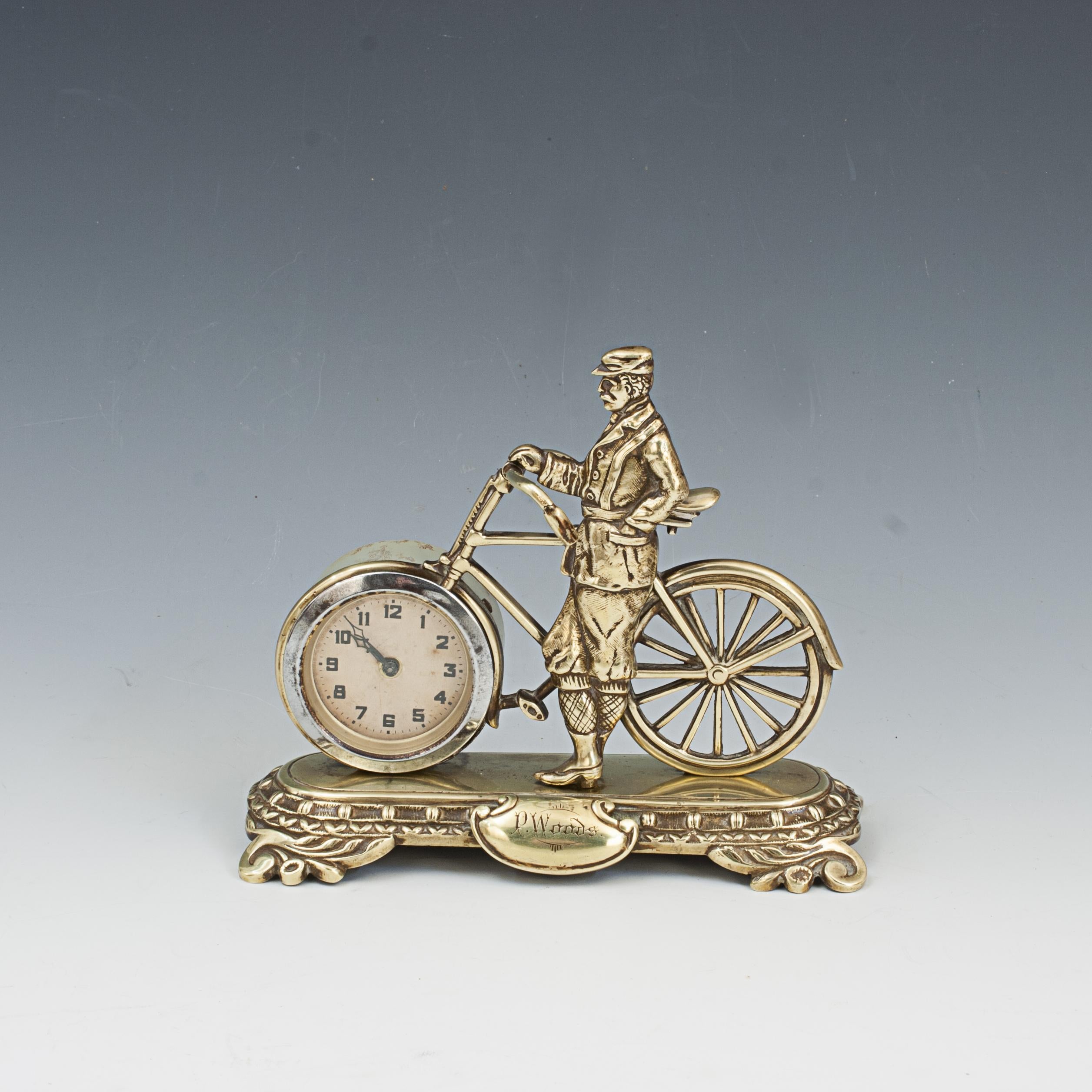Antique Novelty Desk Cycling Clock.
An unusual late 19th Century novelty bicycle clock mounted on a brass base. The gilt-brass bike has a 6 cm clock as a front wheel, clock with black Arabic numerals. The bicycle has been well put together and is
