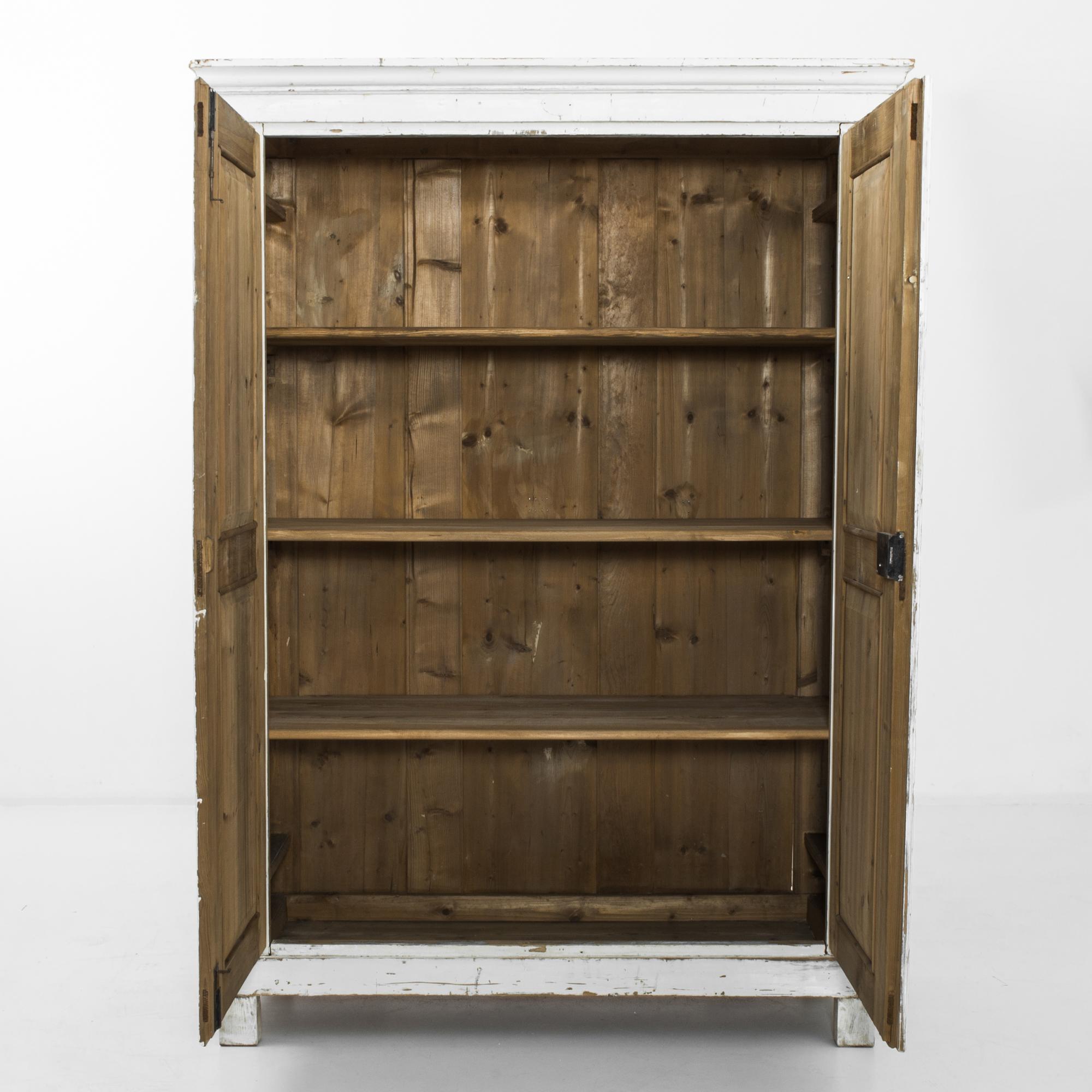 This wooden armoire with crown molding was made in the former Czechoslovakia. Originally painted white, the armoire displays a time-worn patina, which reveals the golden brown hue of the wood beneath and evokes the rustic charm of the countryside.
