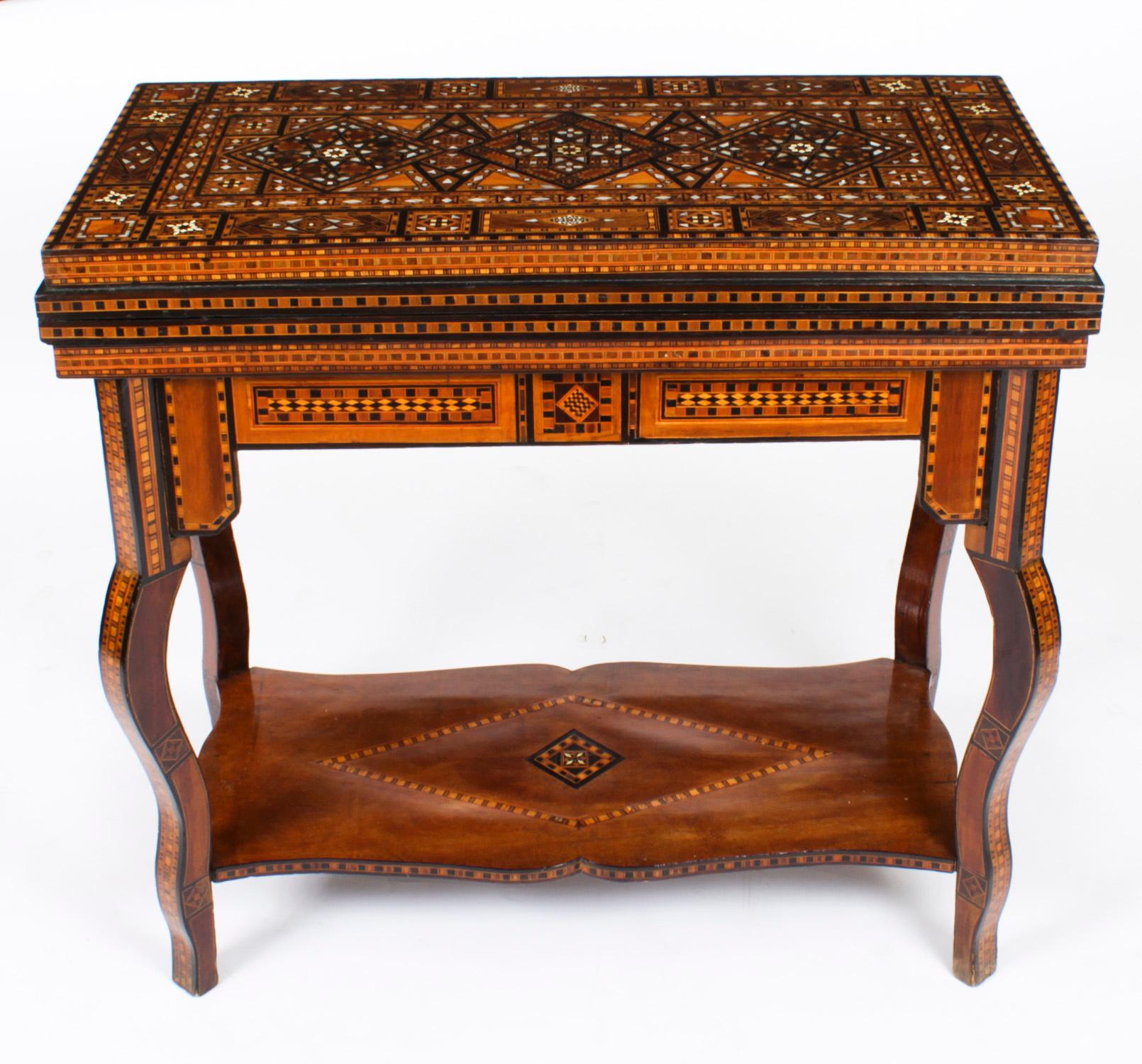 Cette table de jeu en damas syrien richement incrustée date des environs de 1900 et présente de multiples incrustations géométriques et asymétriques de divers spécimens de bois
 
Le couvercle à charnière s'ouvre pour révéler un intérieur incrusté