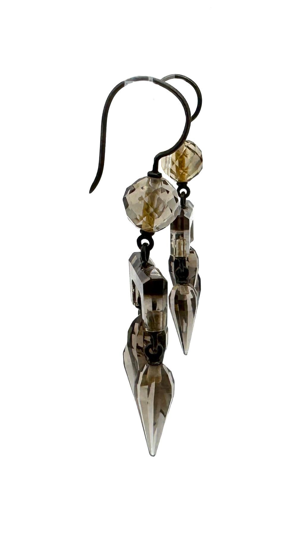 Questi eleganti e ben proporzionati orecchini pendenti in quarzo fumé sono stati creati nel 1875 circa.
Gli orecchini sono disegnati secondo il gusto del revival archeologico che raggiunge il suo apice in quel momento. Le cime argentate scivolano