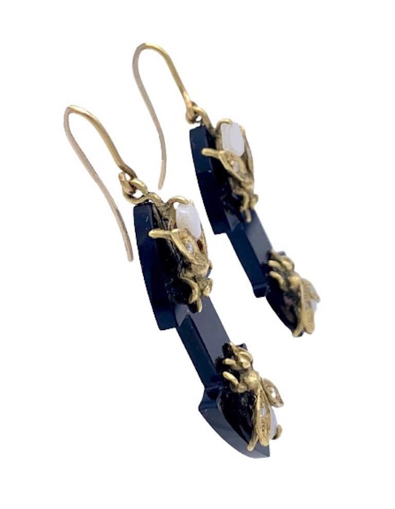 Diese ungewöhnlichen baumelnden Ohrringe sind aus Onyx geschnitzt. Auf jeden Ohrring sind zwei goldene Fliegen genietet worden. Der Körper der Fliegen ist aus Opal-Cabochons gefertigt, jeder Flügel ist mit einem Diamanten besetzt.
In der