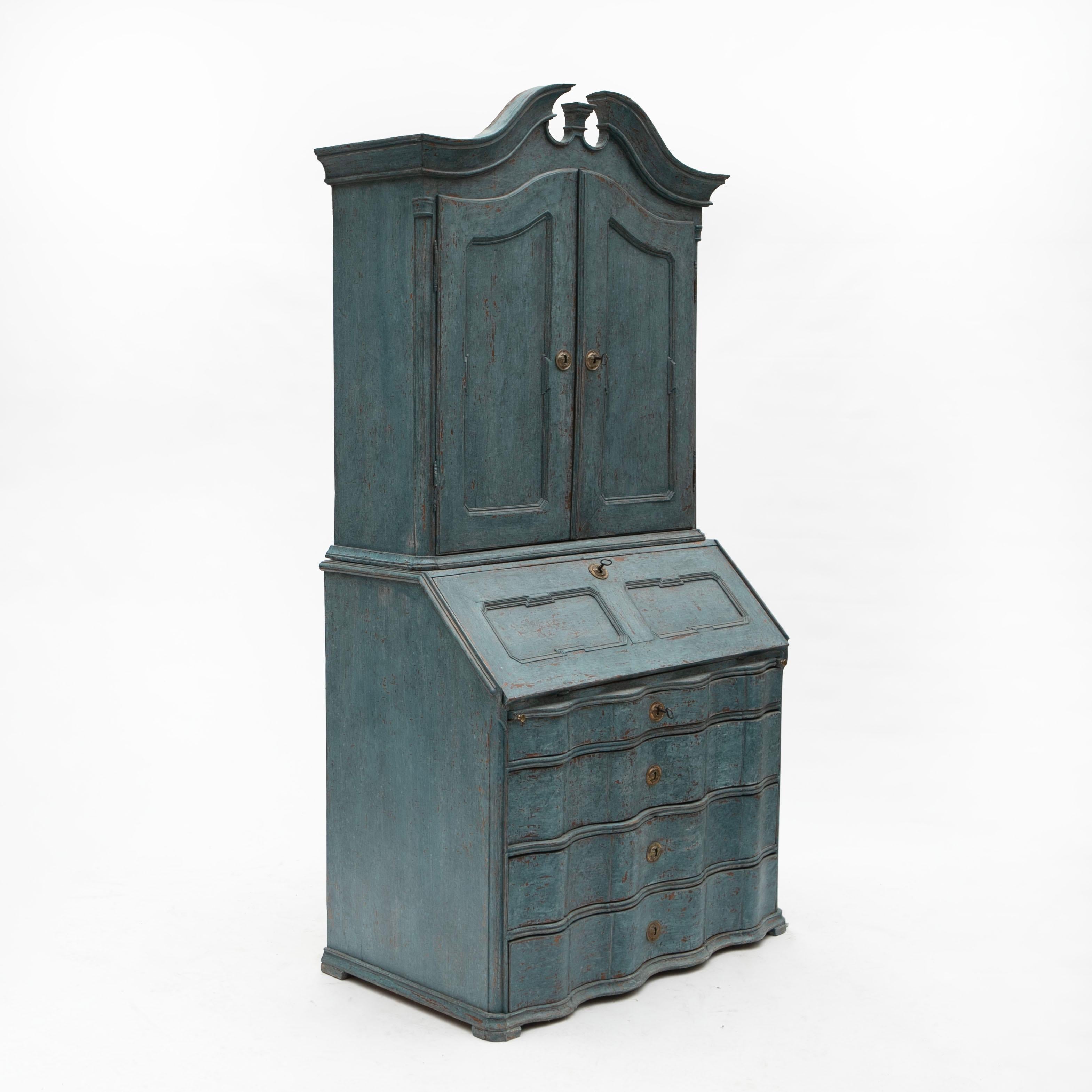 18th Century Danish Baroque period secretary cabinet in two parts. Crafted in oak, painted in a beautiful blue color and a dark grey interior.

Upper cabinet with curved crown and a decorative carved swan neck pediment over double doors the follows