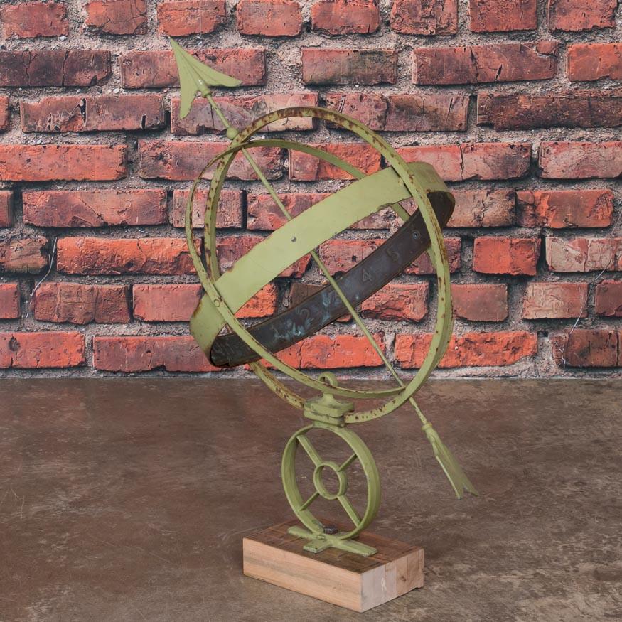 This vintage green painted globe shaped garden ornament, called an armillary, is made up of metal bands, pierced by an arrow and supported by a mounting bracket. These 