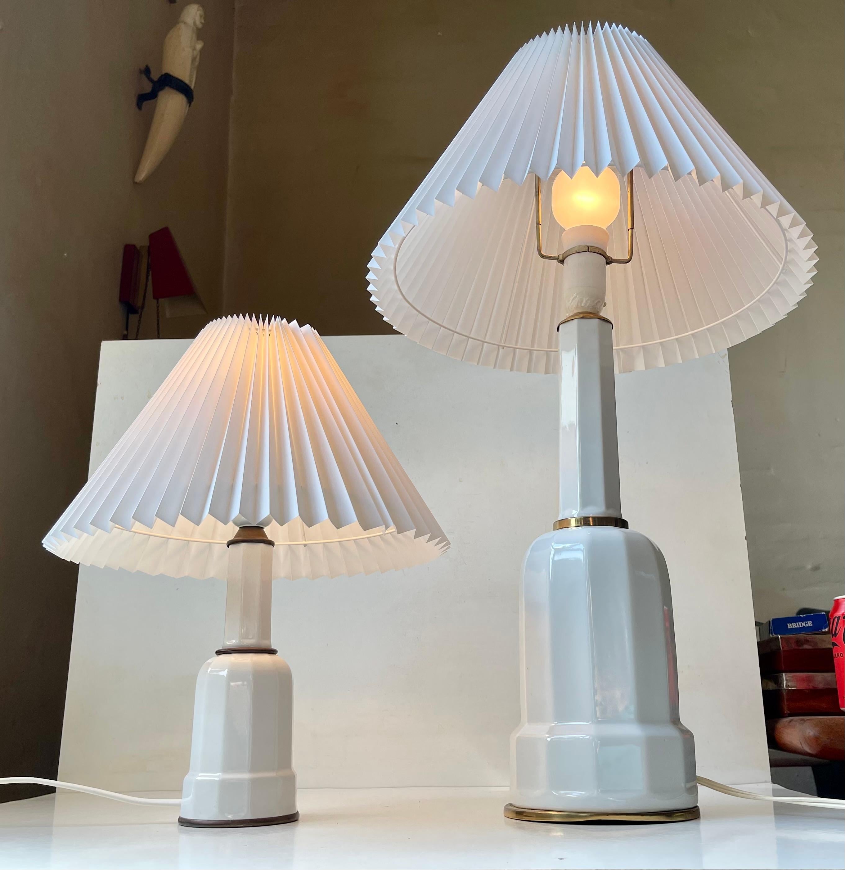 A matching 'small' and large example of the original Heiberg table lamps. They are made from white glazed porcelain featuring accents in patinated brass. The name Heiberg derives from a 1830s painting by Wilhelm Marstrand of the Heiberg family