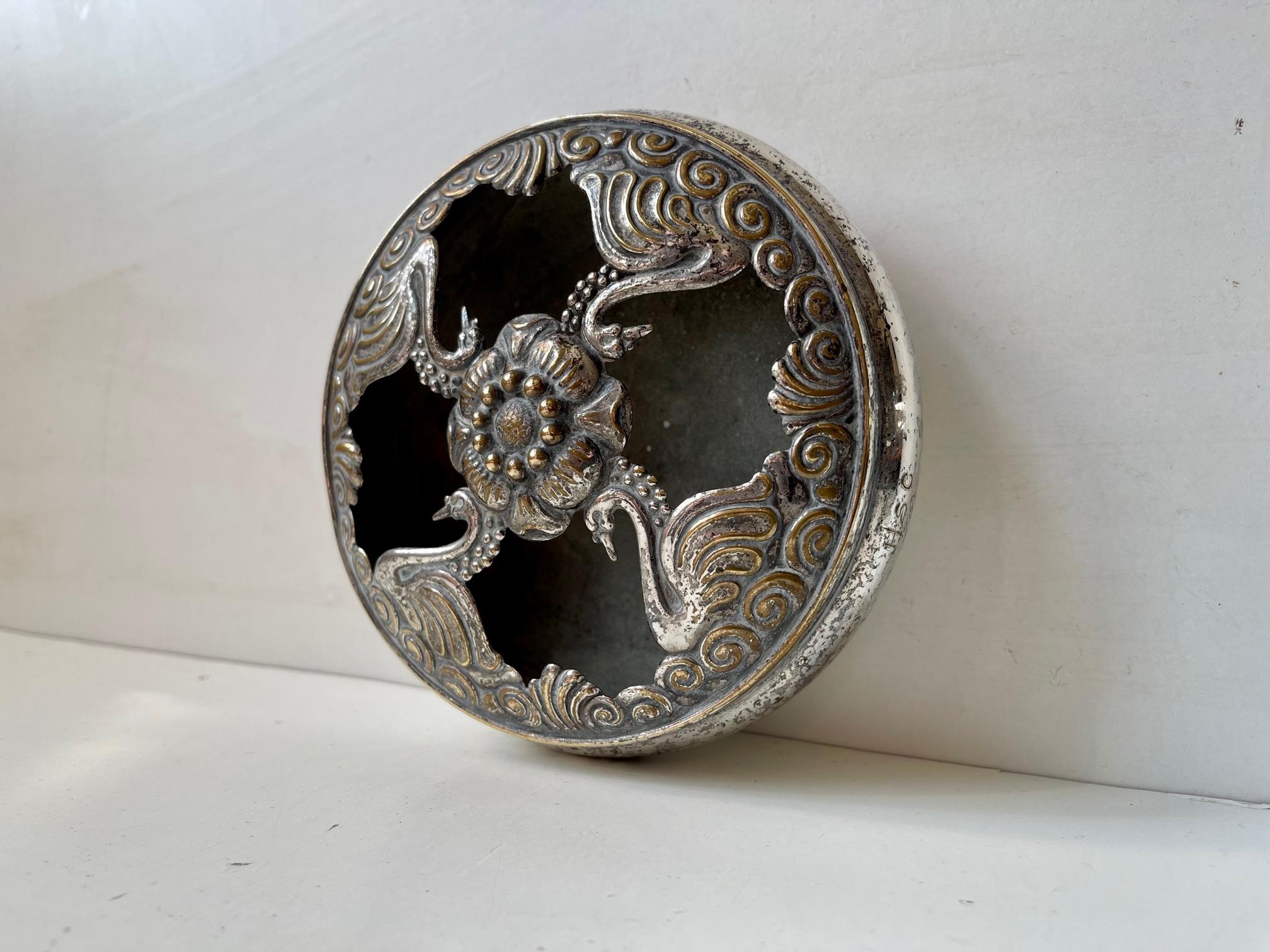 Un bol à encens décoratif ou un pot-pourri avec une maille supérieure perforée avec des cygnes. Il est fabriqué en laiton et partiellement plaqué argent. Elle a été conçue et fabriquée par la société de joaillerie AT&T au Danemark vers 1910-25.