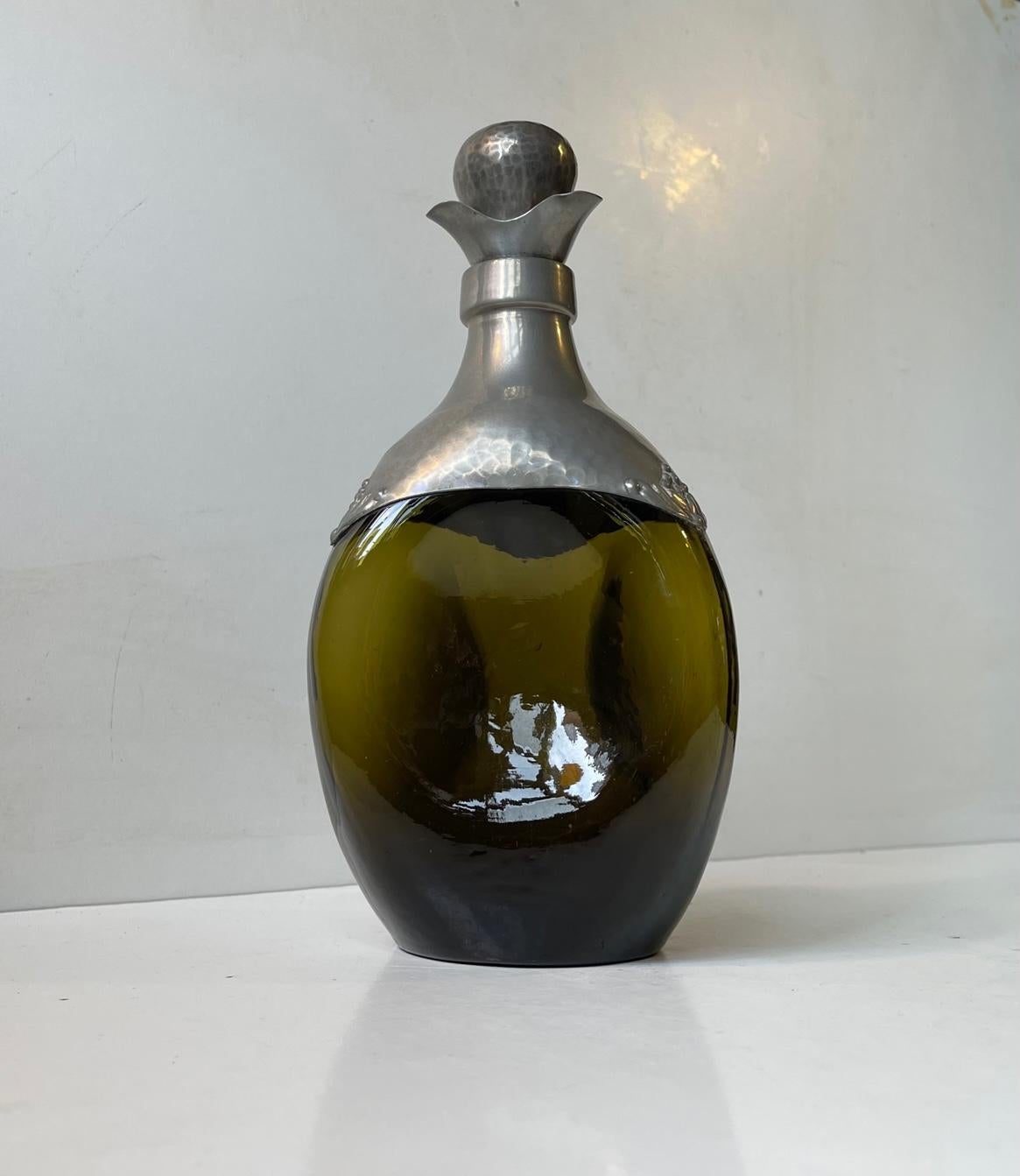 A rare beautiful decanter in green hand-blown glass. Decorated with hand-set/fitted panels of lightly hammered pewter. Original stopper in pewter and cork. Distinct Danish Jugendstil - art nouveau styling reminiscent of Thorvald Bindesbøll. Made in