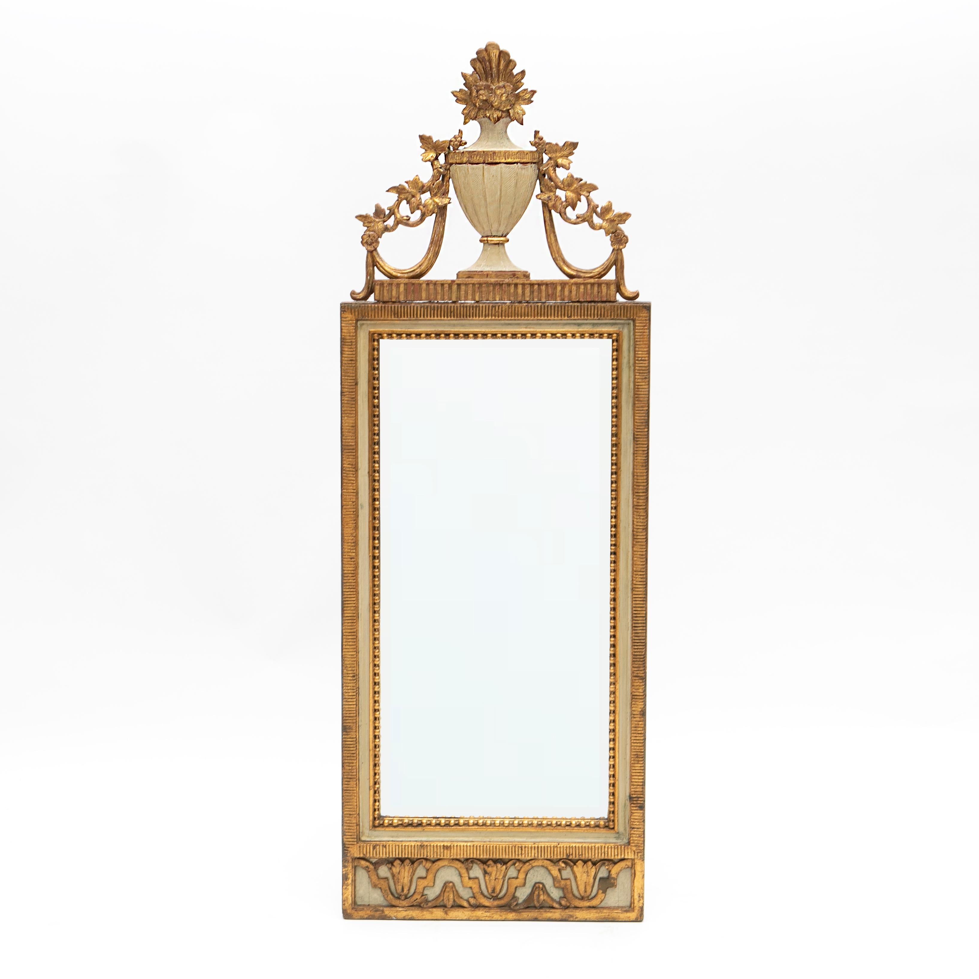 A Danish Louis XVI period carved giltwood wall mirror in original condition. 
Features a bevelled mirror in a light gray and gilt carved frame with flutings surrounded by a carved bead border. At the top a carved vase and foliage.

The light