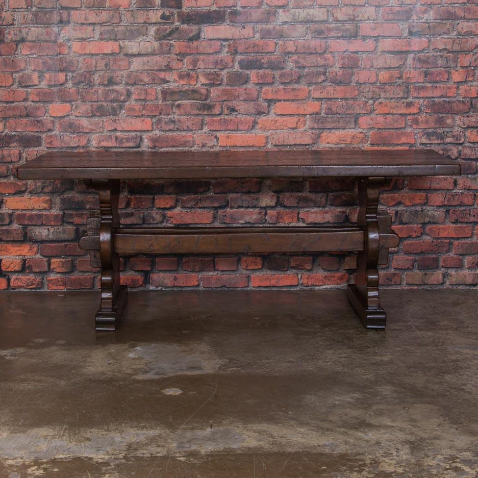 This solid dark oak trestle table glows with a rich distressed patina that compliments the country style. The two stretchers anchor the elegant thick scrolled legs. The table has been professionally restored, is very stabile and ready for daily use.