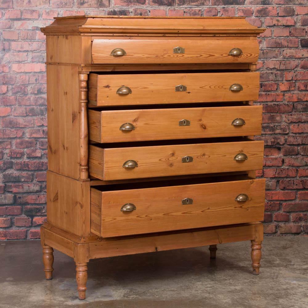 The turned columns and sweeping crown add a refined touch against the clean lines of the simple Danish styling on this pine chest of five drawers. This piece has been professionally restored and the pine has been given a wax finish bringing out the