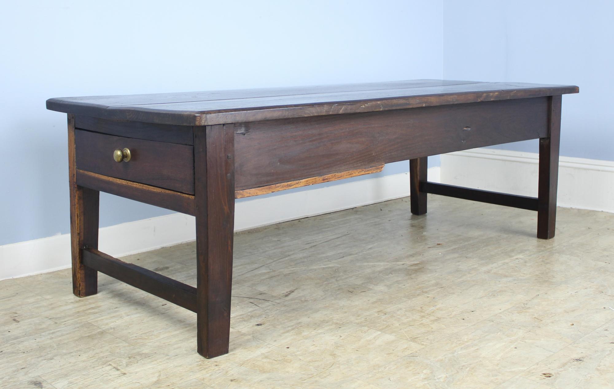A longer antique coffee table in dark, rich chestnut with yellow stripey grain on the base, mimicking walnut. One deep storage drawer at the end. Interesting shaped apron and cleated top. A Classic!