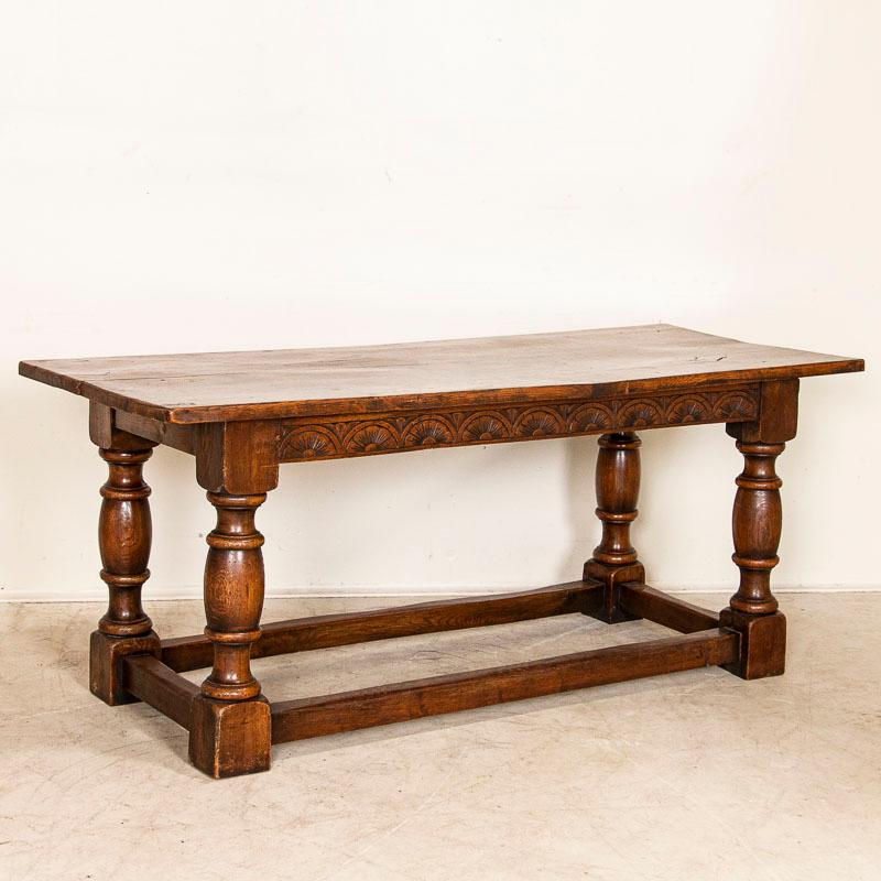 Heavy turned legs with a trestle base create the great lines in this solid oak refectory or library table from France. The decorative hand-carved skirt adds depth and drama as well. Examine the close up photos to appreciate the dark patina of the