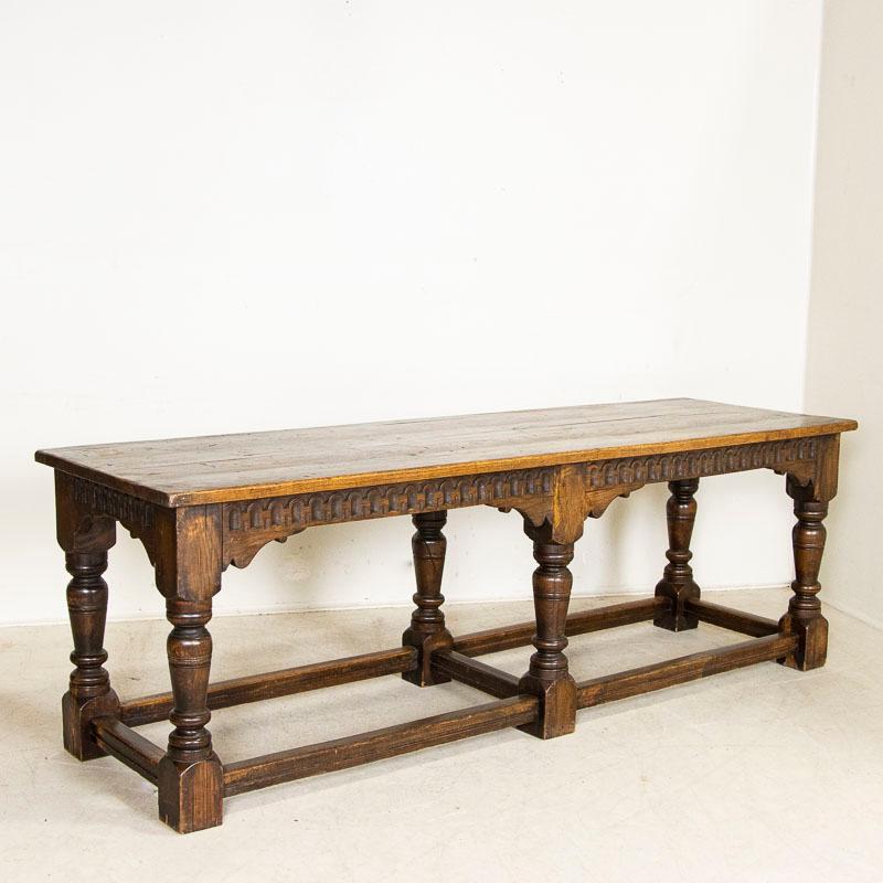 Heavy turned legs with a trestle base create the great lines in this solid oak refectory or library table from France. The decorative hand-carved skirt adds depth and drama as well. Examine the close-up photos to appreciate the dark patina of the
