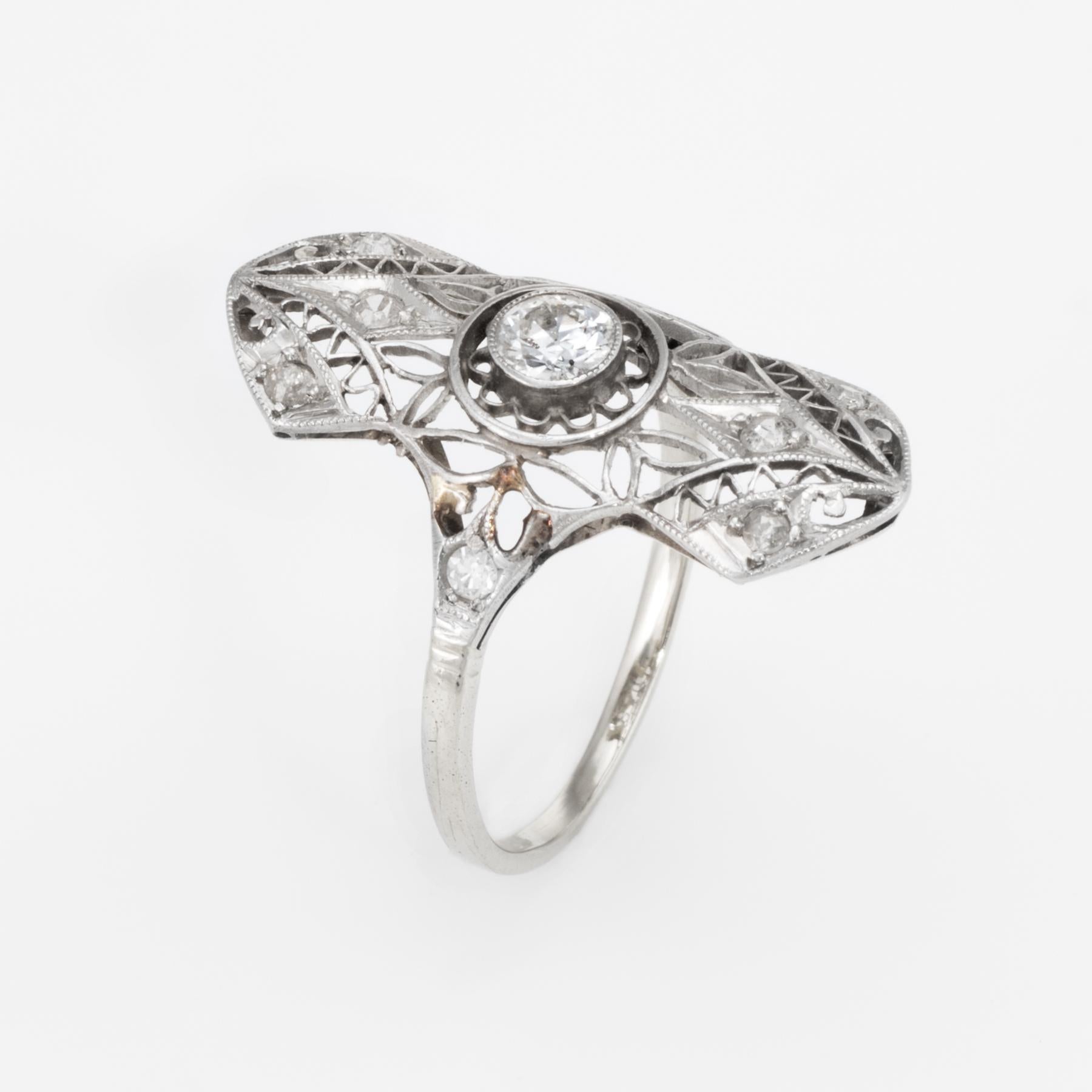 Fein detaillierter Ring aus der Art-Déco-Ära (ca. 1920er bis 1930er Jahre), gefertigt aus 14 Karat Weißgold. 

Ein zentral montierter Diamant von schätzungsweise 0,20 Karat im alten europäischen Schliff ist mit 8 Diamanten von schätzungsweise 0,02
