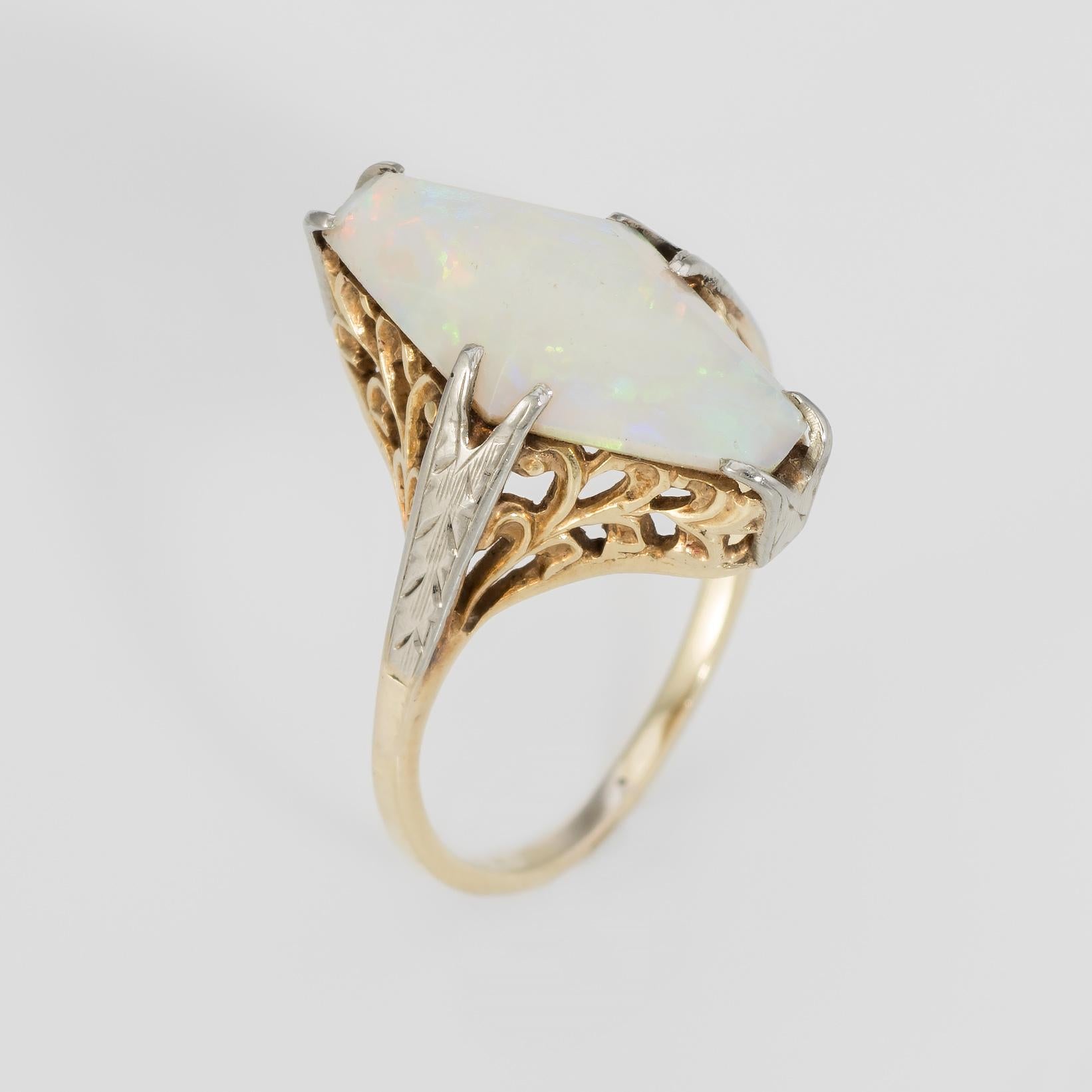 Finely detailed Art Deco era ring (circa 1920s to 1930s), crafted in two tone 14 karat yellow and white gold. 

Triangular cut cabochon opal measures 16mm x 8mm (estimated at 4 carats). The opal displays a vivid color matrix from green to orange,