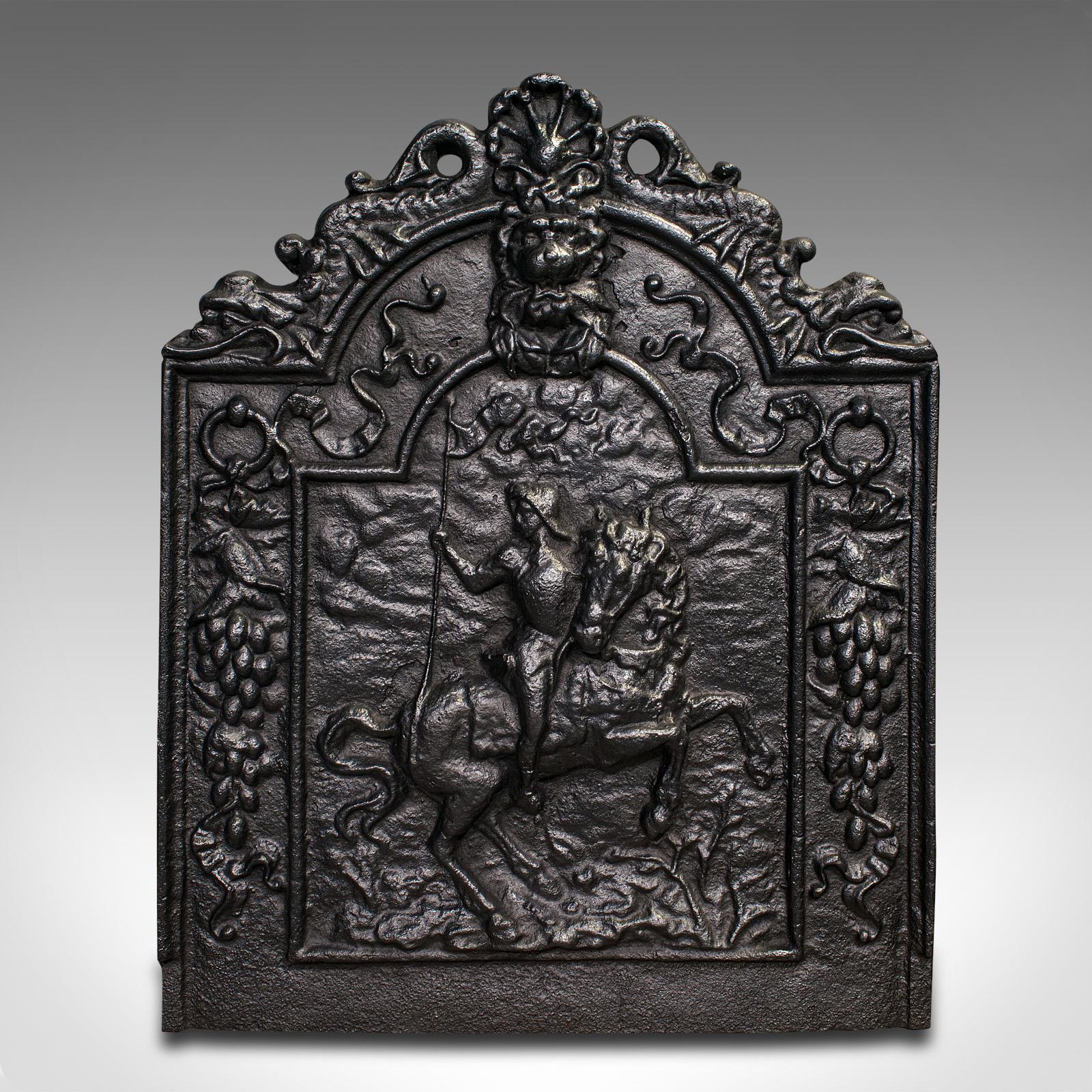 This is an antique decorative fire back. An English, cast iron fireplace backrest, dating to the late Victorian period, circa 1900.

Pleasingly cast with a mounted rider and old English motif
Displays a desirable aged patina throughout
Cast iron