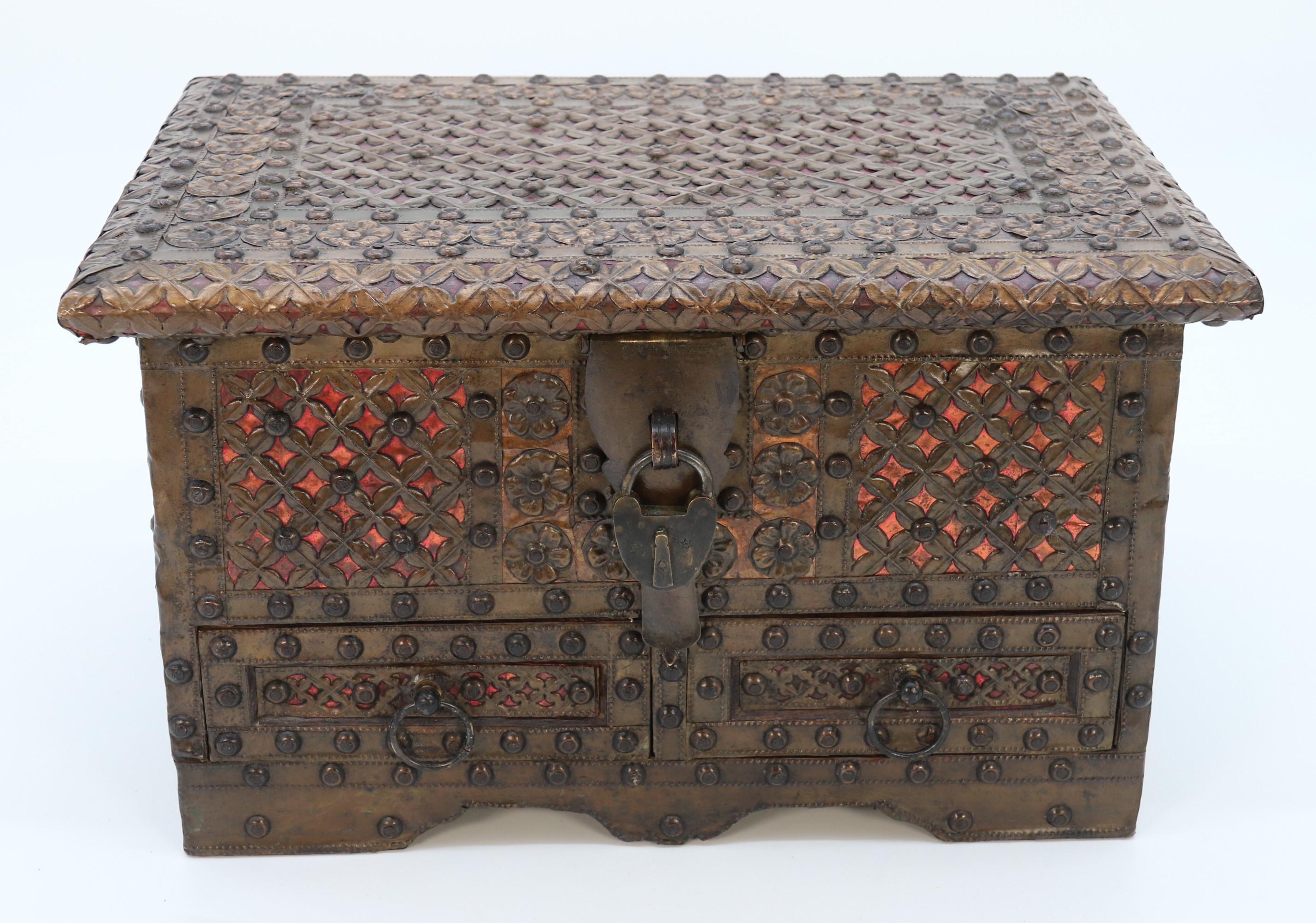 
This remarkable and small beautifully proportioned Zanzibar chest is a highly decorative piece made from a mixture of teak and other various woods. This sturdy little chest or strongbox Is very ornately mounted with pierced and embossed brass and